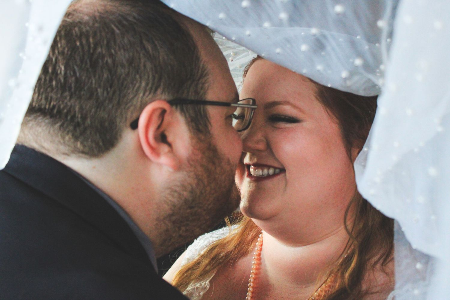 Close up shot of a happy newlywed couple sharing an intimate moment under a white veil.