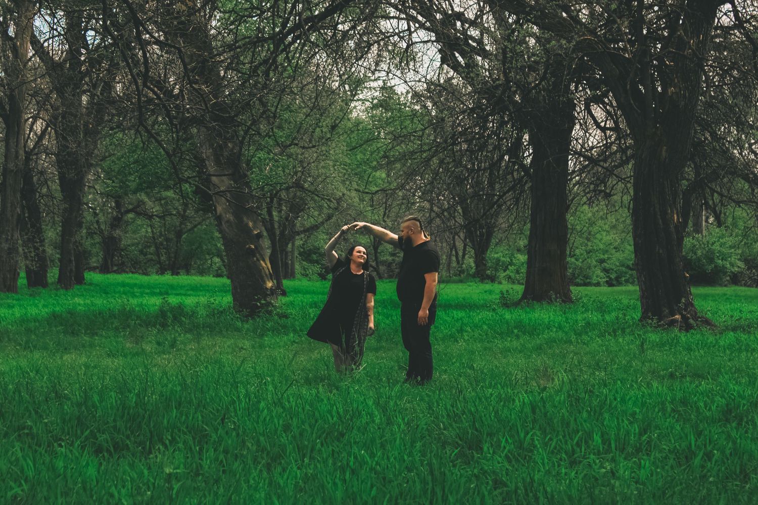 Two people walking together through a lush green field surrounded by trees on a misty day.