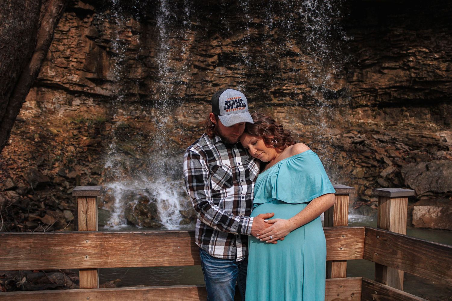A couple embraces in front of a rustic rock wall with smoke wisping through the air near wooden lanterns.