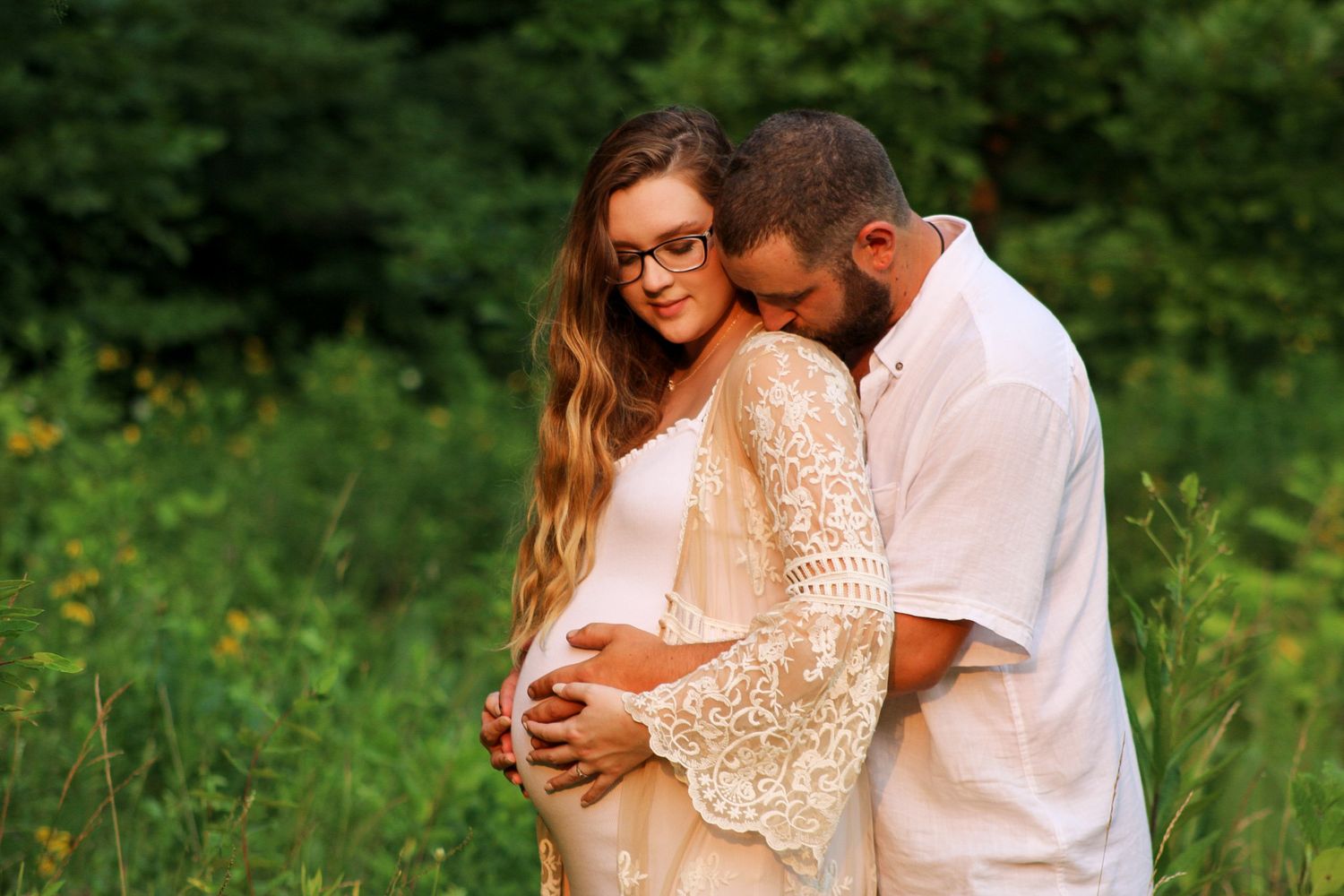 A couple embraces in a sunlit meadow with wildflowers, sharing a tender moment together.