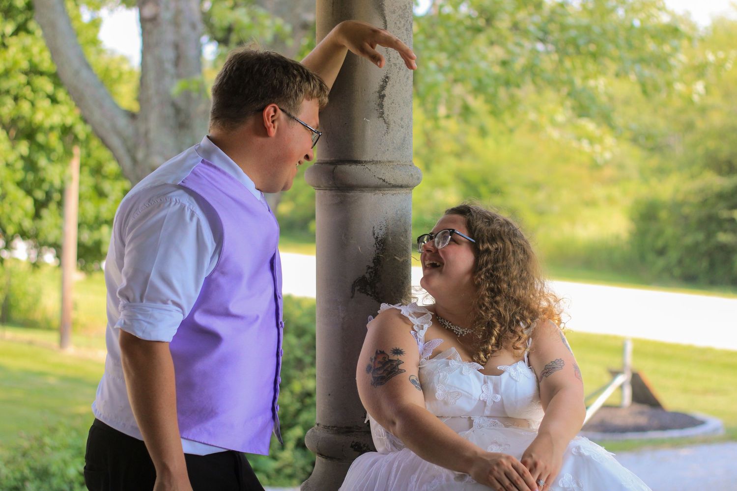 Two people pose for a romantic moment by a stone pillar in an outdoor garden setting during sunset.