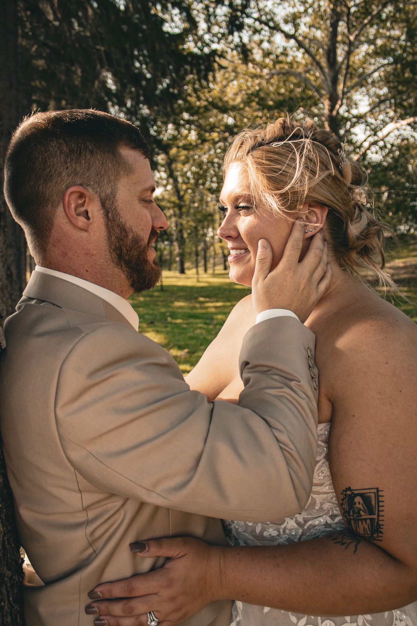 A loving couple shares an intimate moment outdoors during their wedding, with sunlit trees in the background.