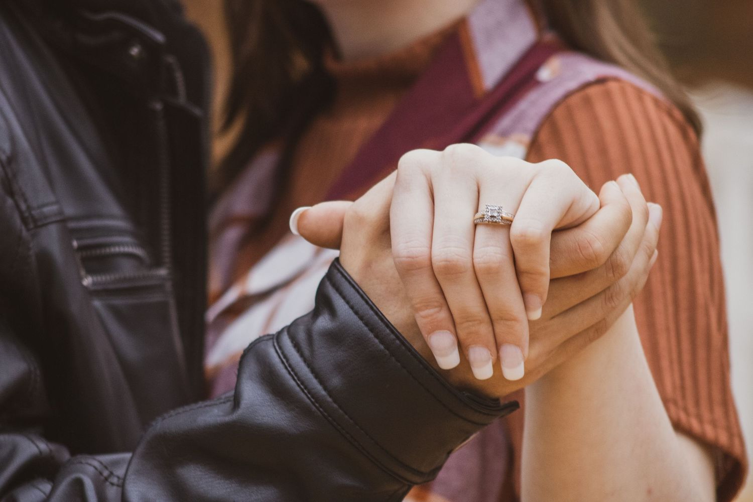 Two hands clasped together, with an engagement ring glinting in soft light on one finger.