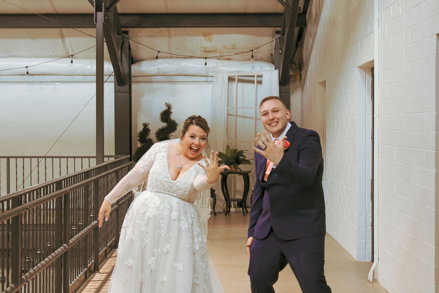 Fun and joyful newlywed couple playfully pose together in indoor hallway.