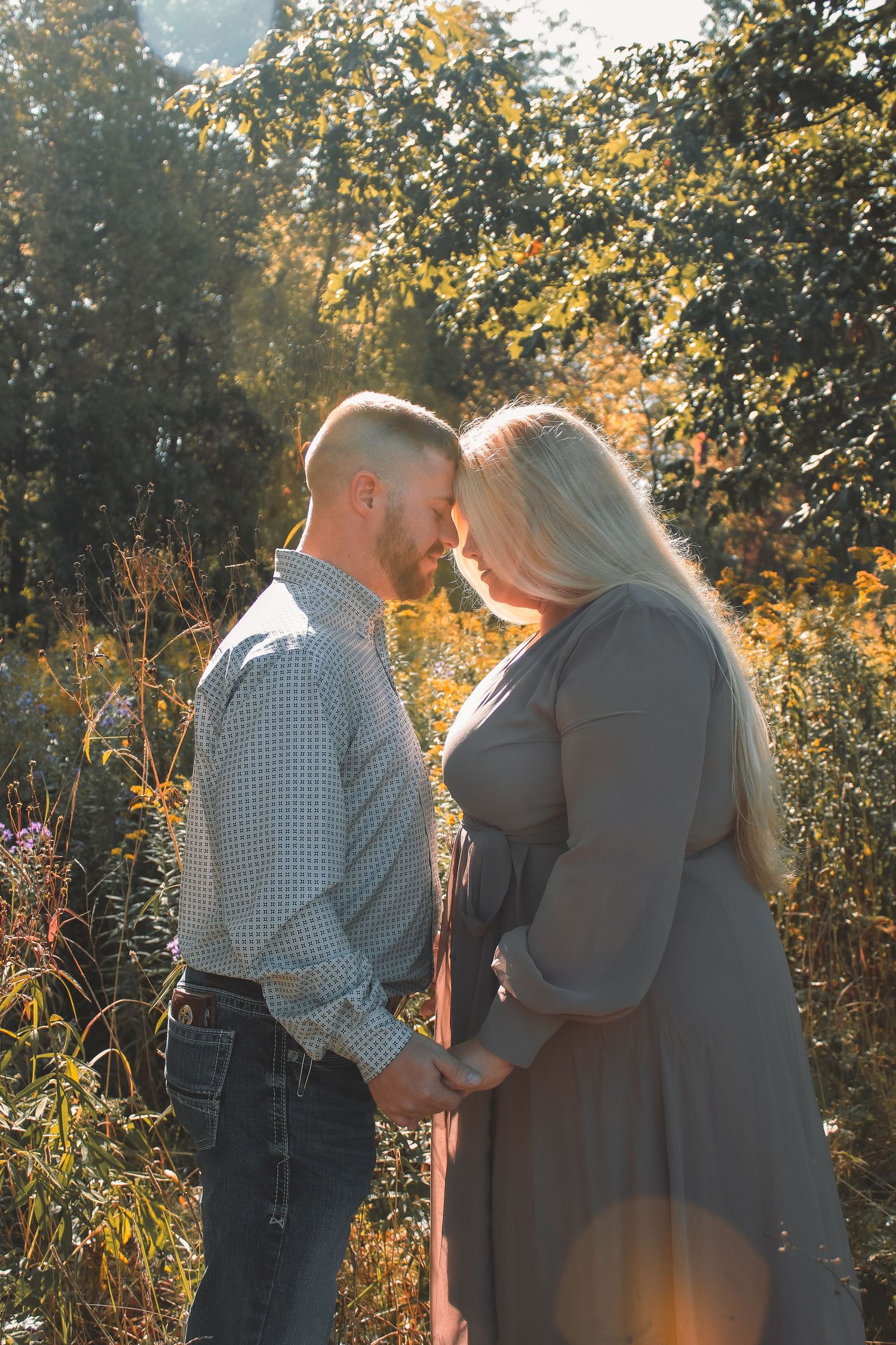 A couple shares an intimate moment while holding hands in a sunlit autumn forest setting.