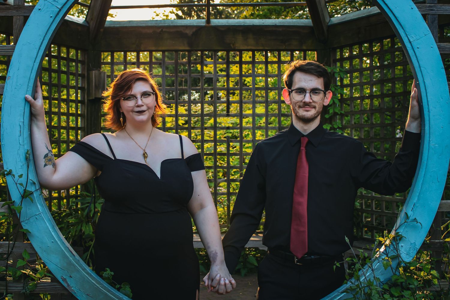 A couple poses together inside a large circular blue garden frame against a latticed backdrop.