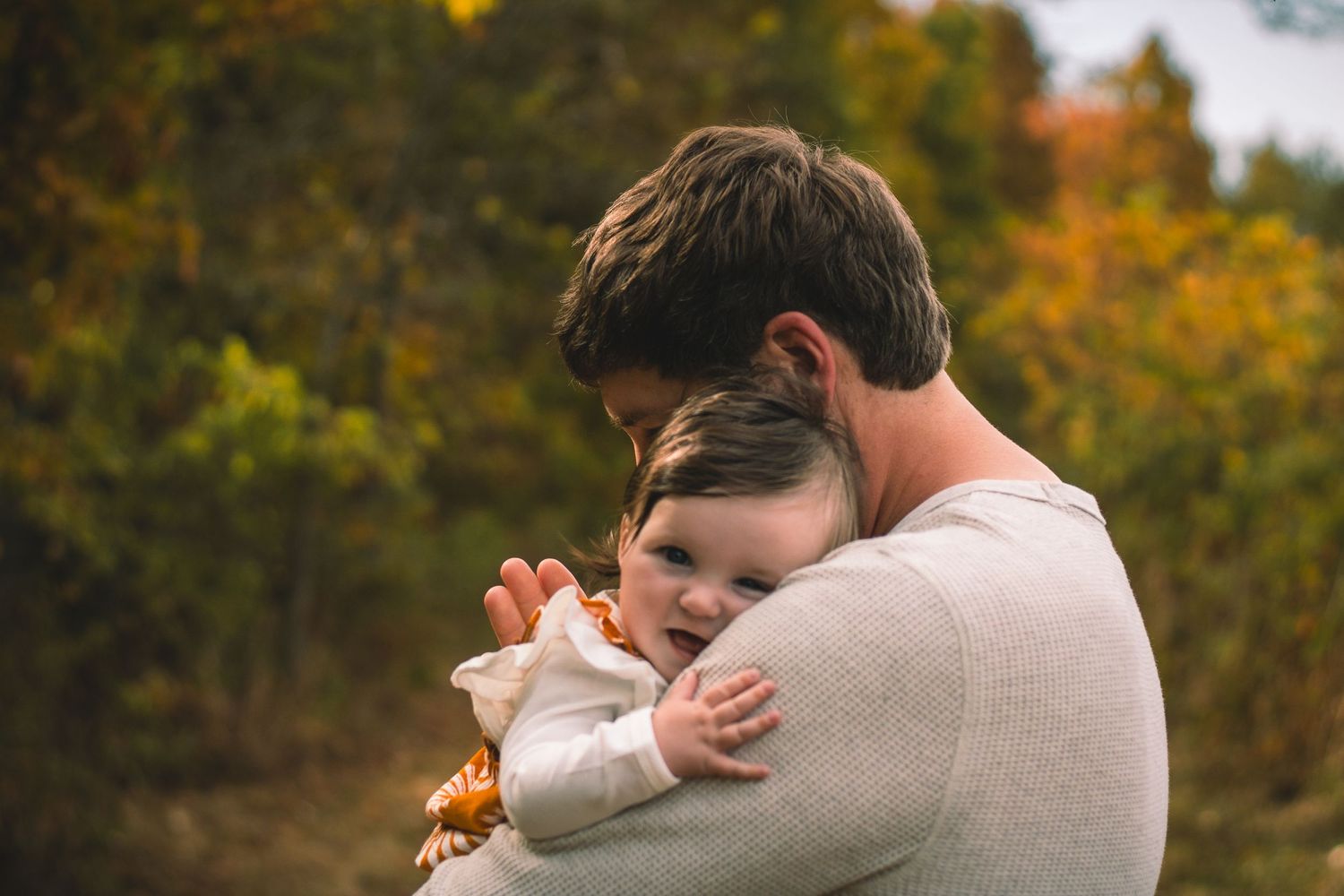 Tender moment between parent and child embracing outdoors with autumn foliage in background.