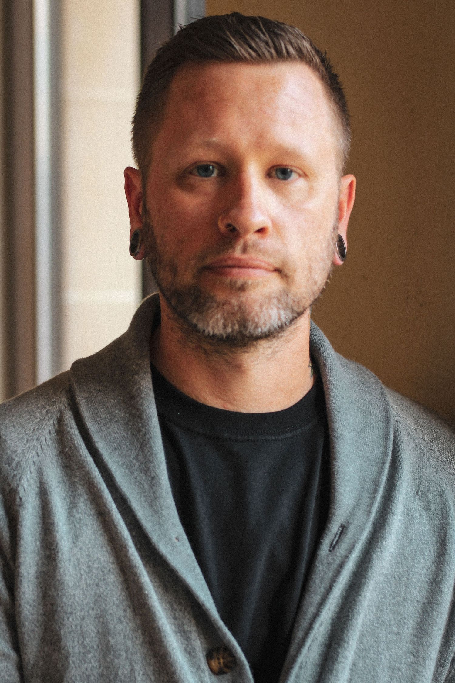Professional headshot portrait of a person wearing a gray cardigan and black shirt against a blurred background.