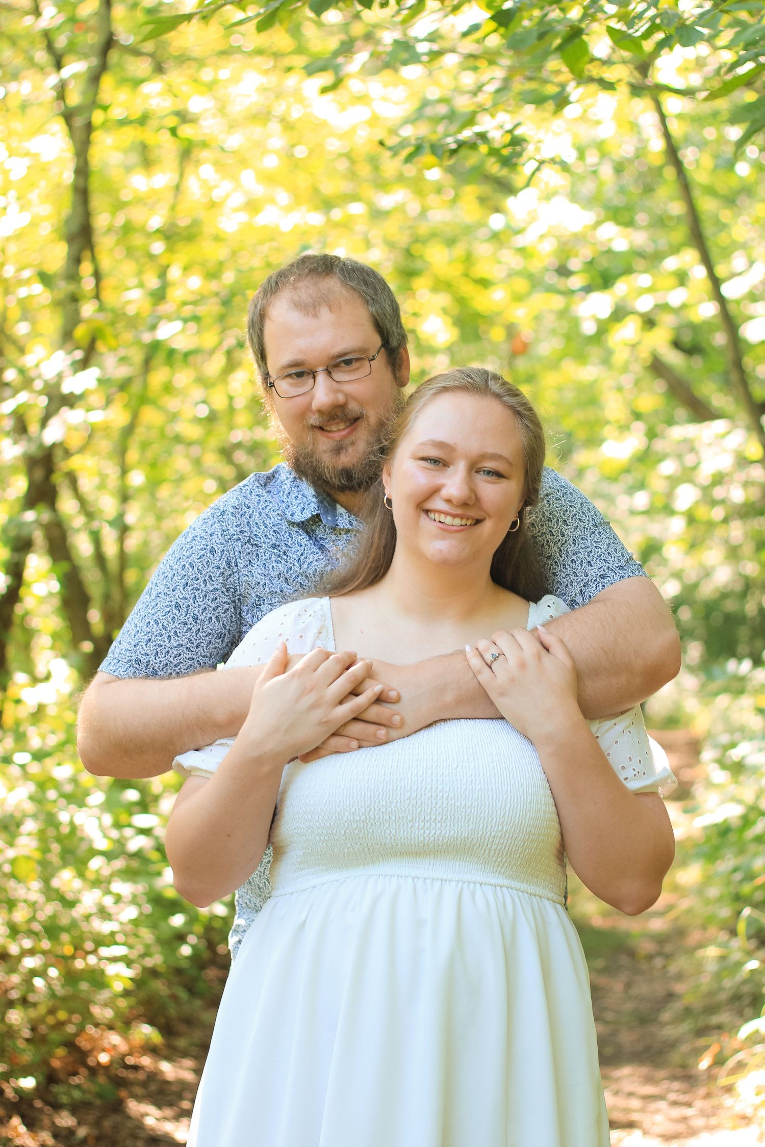 A couple embraces in a sunlit forest setting, with golden foliage creating a warm autumn backdrop.