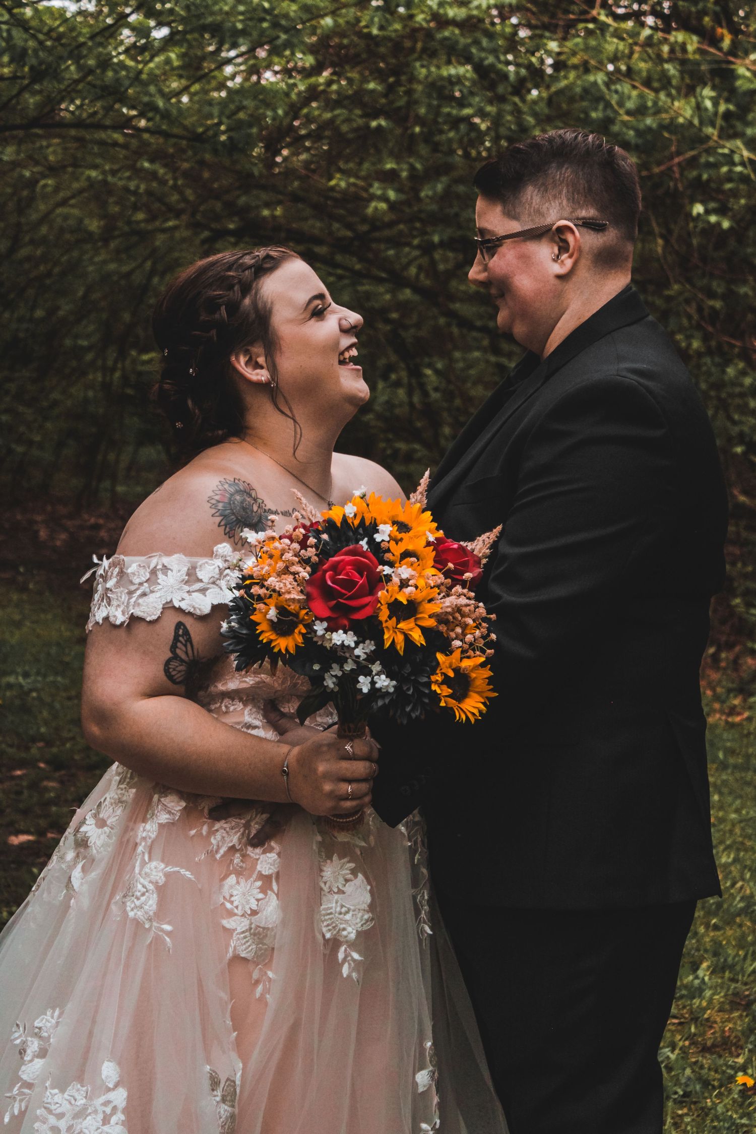 A happy couple shares a candid wedding moment outdoors with a vibrant autumn bouquet of sunflowers and roses.