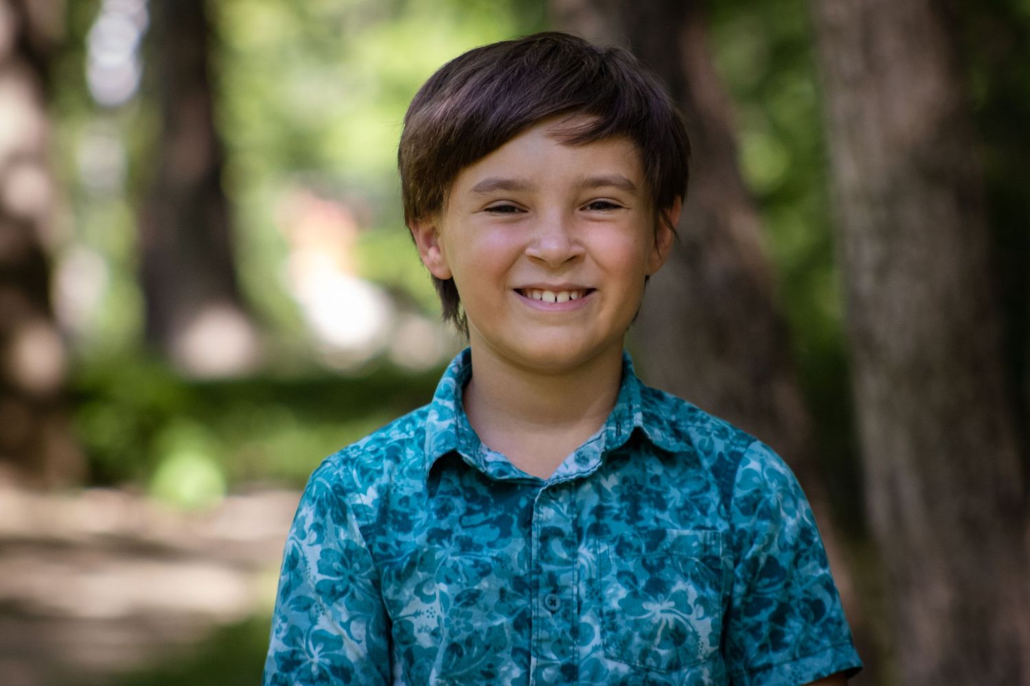 Portrait of youth wearing bright turquoise patterned button-up shirt standing outdoors with blurred forest background.