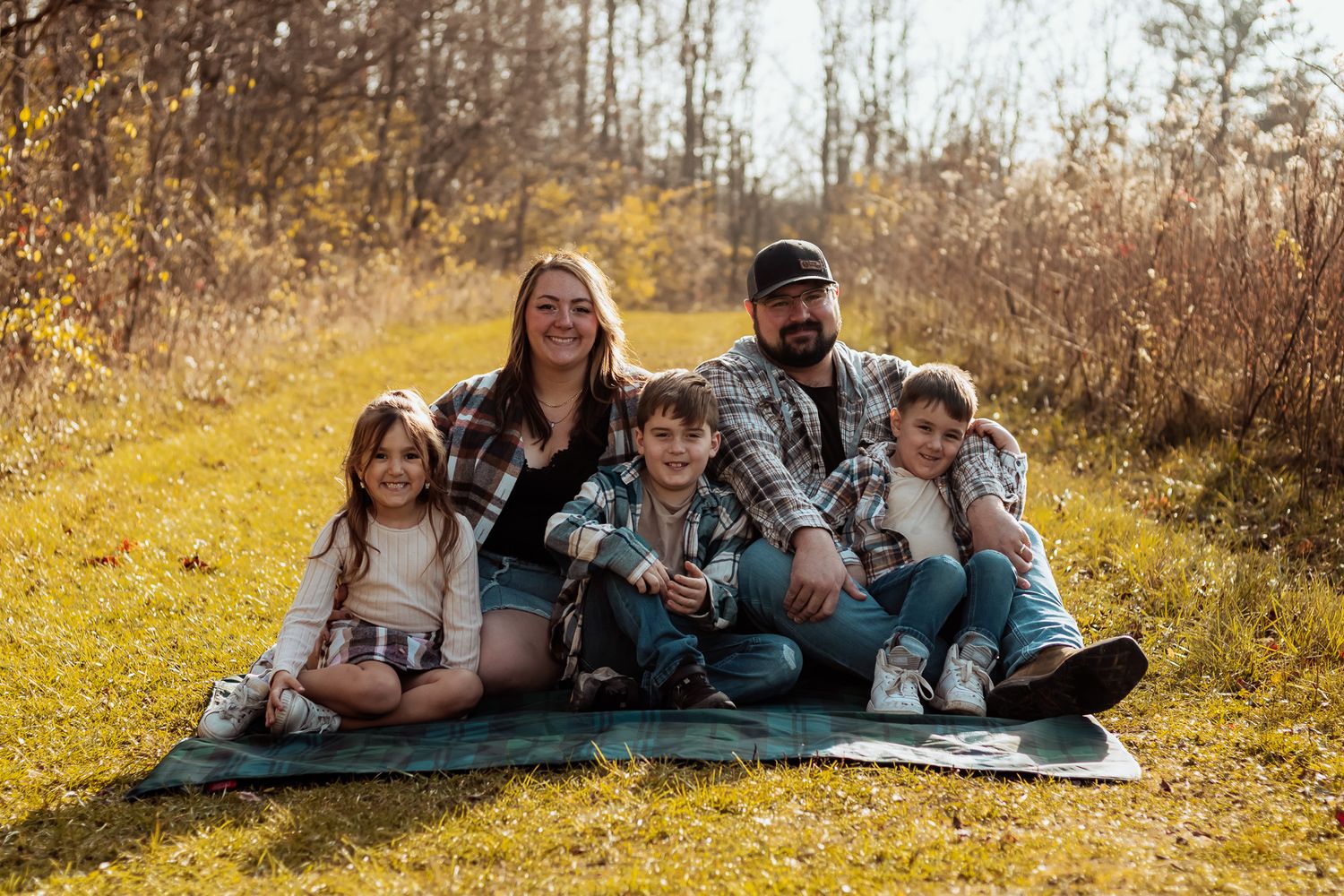 A group enjoying quality time together while sitting on a blanket in a golden autumn field at sunset.