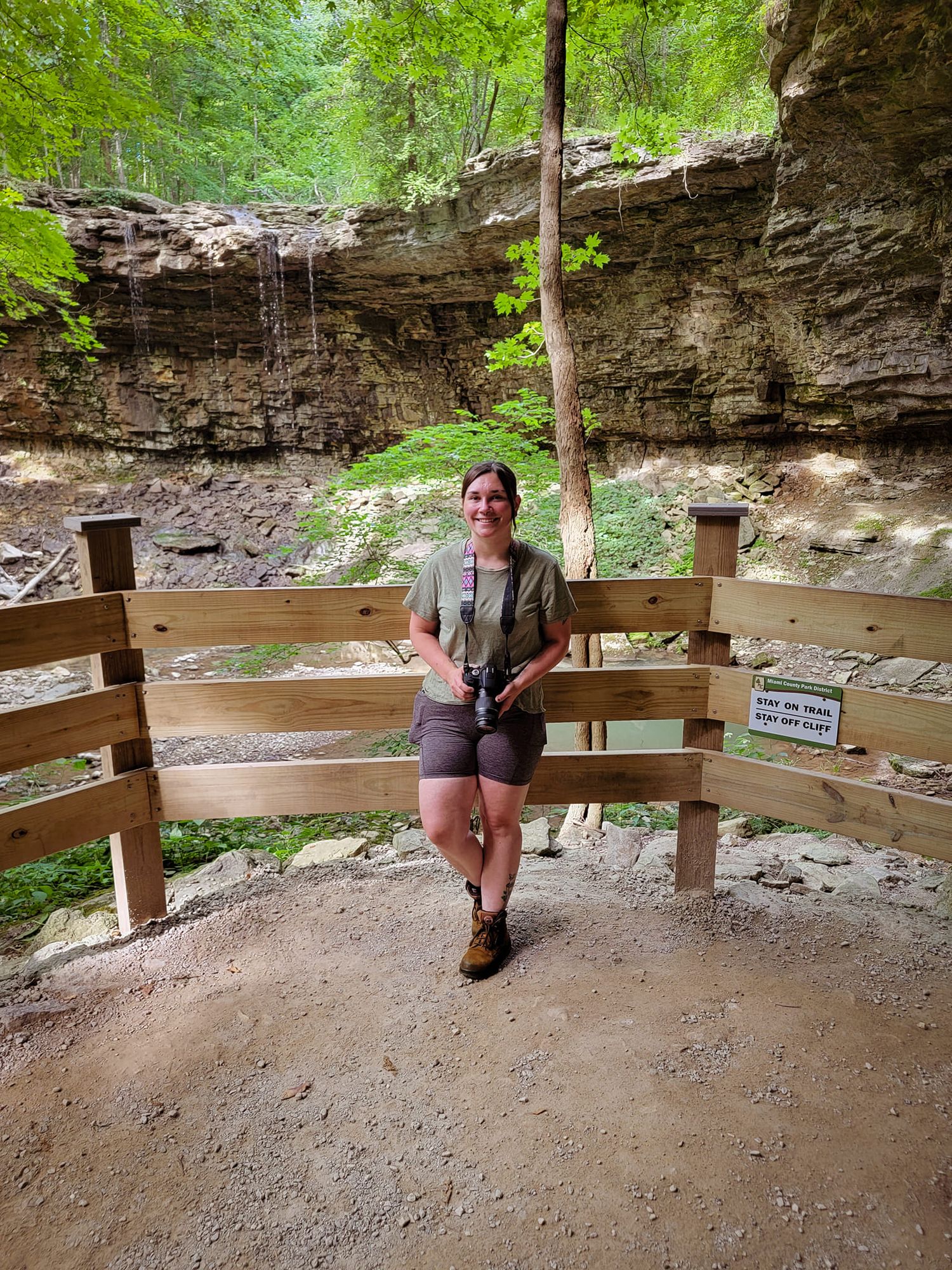 A wooden bench overlooks a scenic creek bed under a natural rock overhang in a state park setting.
