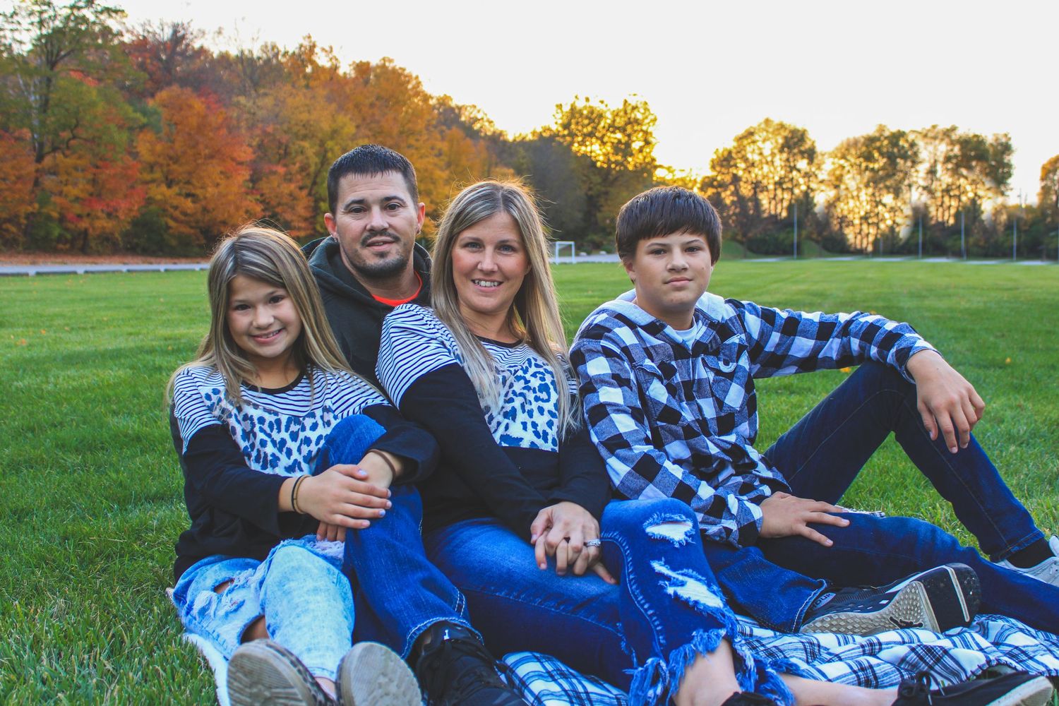 Group poses together on blue blanket during autumn photoshoot in park with colorful fall foliage in background.