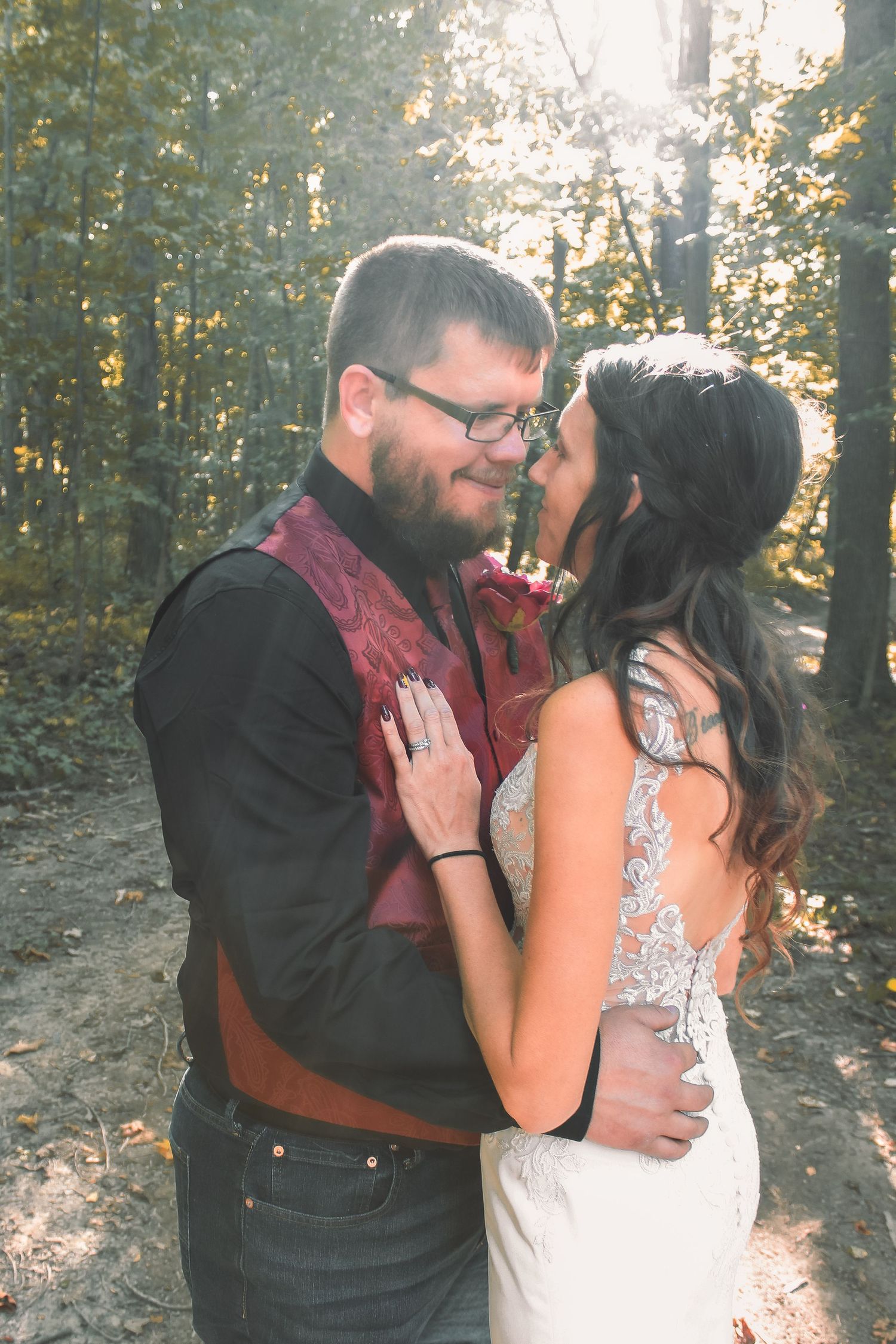 A couple in wedding attire embrace in a sunlit forest setting on their special day.