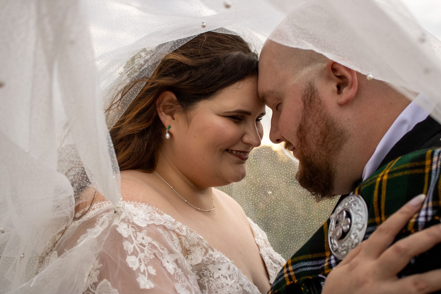 Close-up of newlywed couple sharing an intimate moment under a wedding veil outdoors.