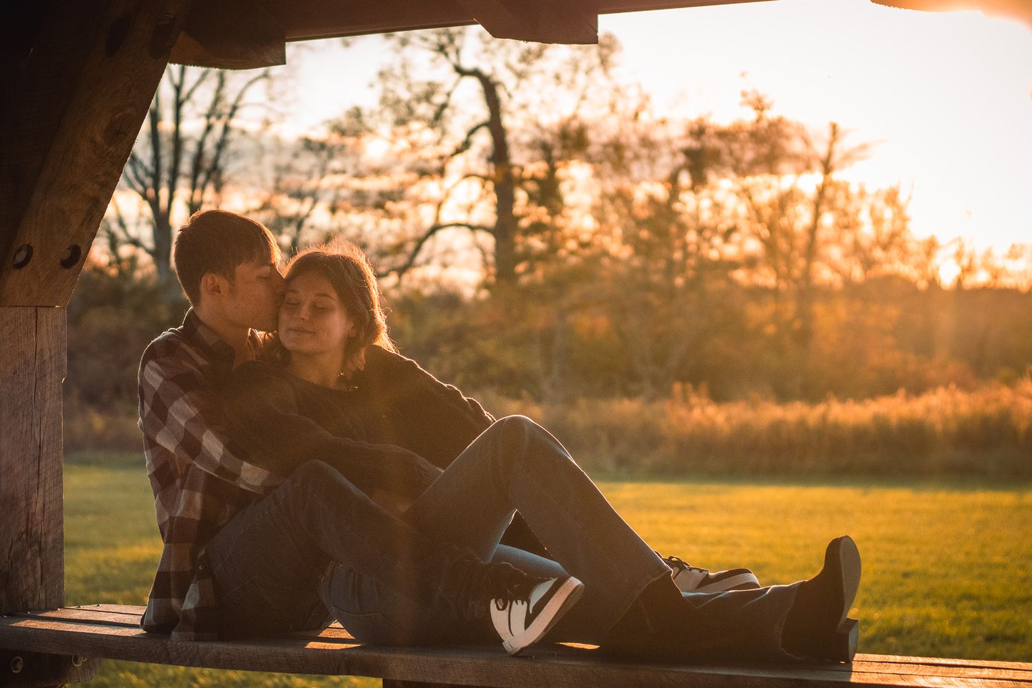 Silhouetted couple sharing romantic moments on a bench during golden hour sunset in a park setting.