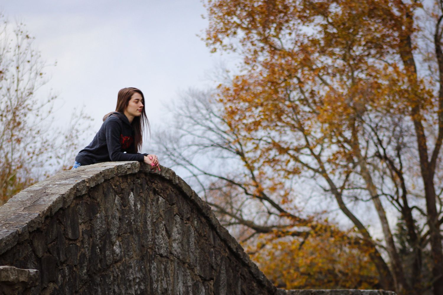 Someone sits atop a large boulder in a park on an autumn day with fall foliage in the background.