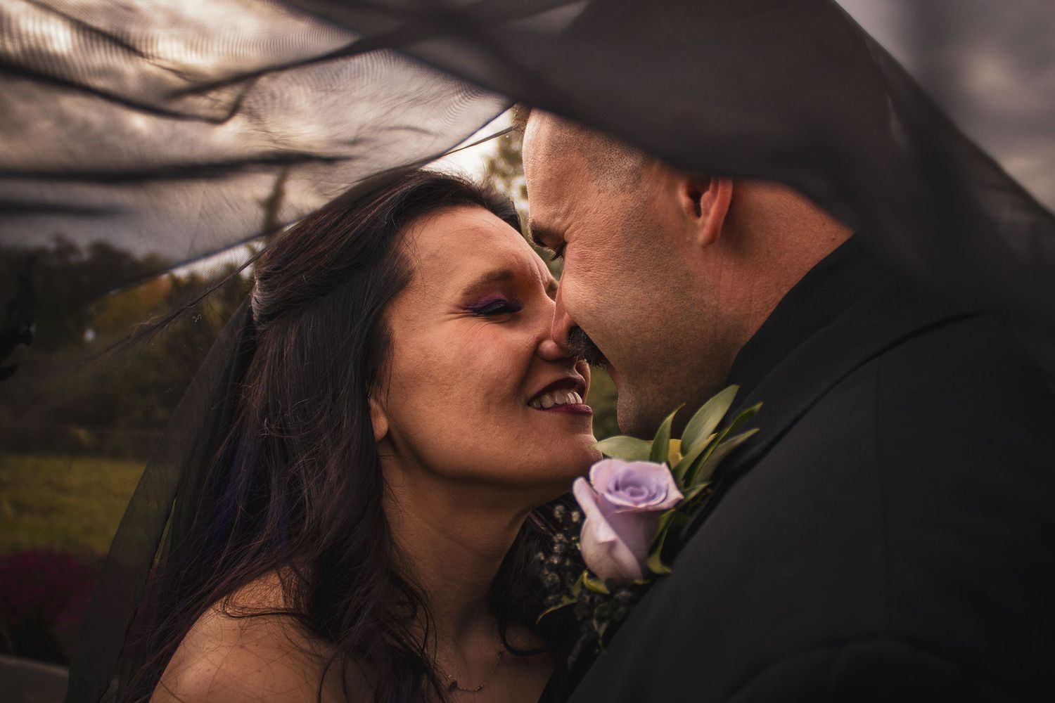 A romantic moment between a couple on their wedding day with a purple rose boutonniere in soft lighting.