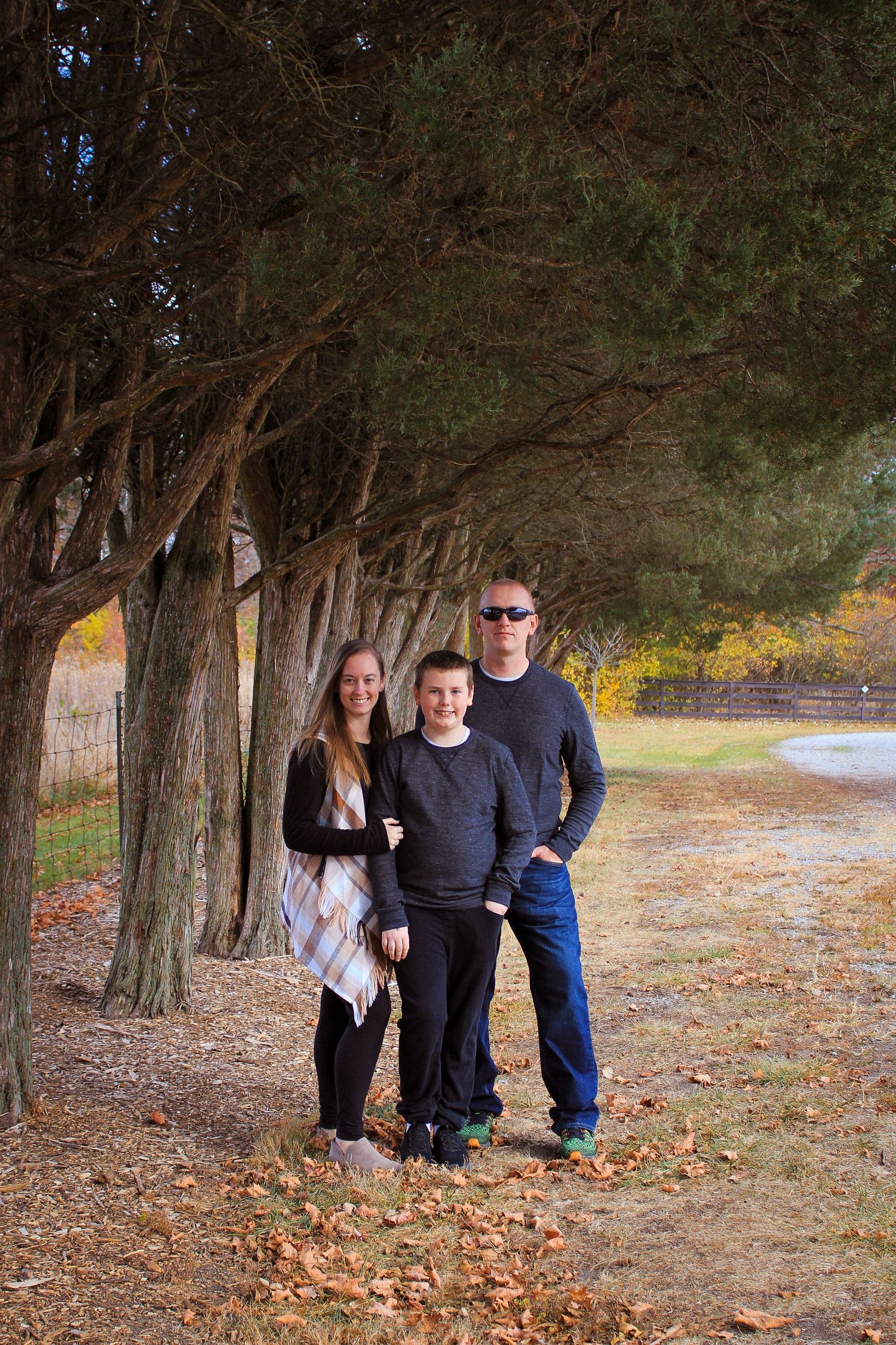 A family poses together on an autumn path lined with trees and fallen leaves on a sunny afternoon.
