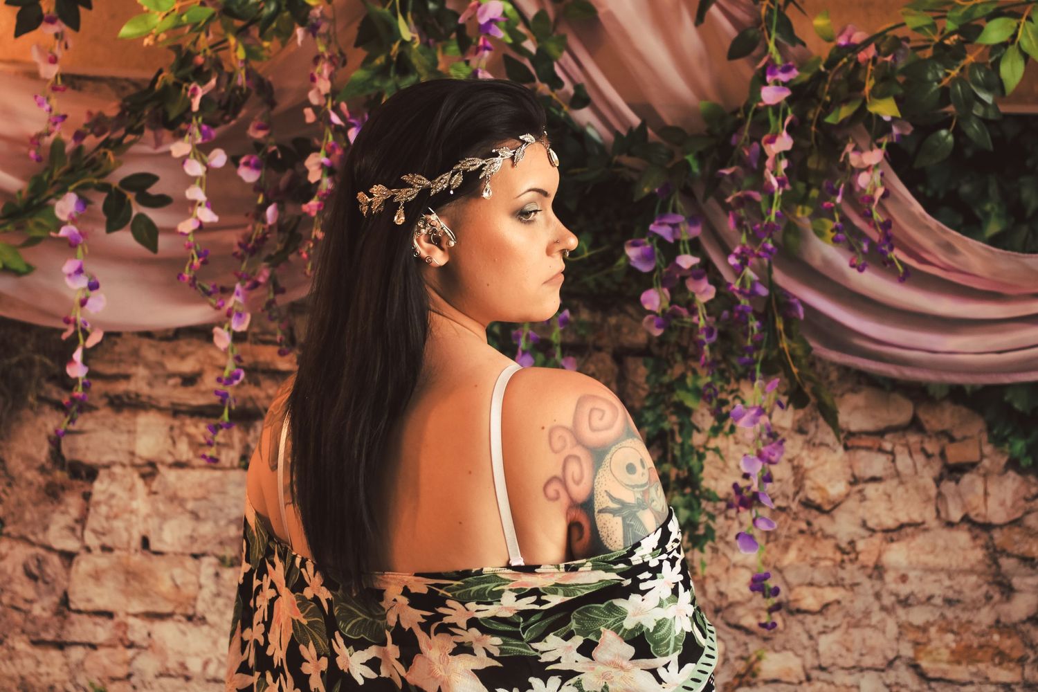 Romantic portrait of woman in floral crown against stone wall with cascading purple wisteria flowers.