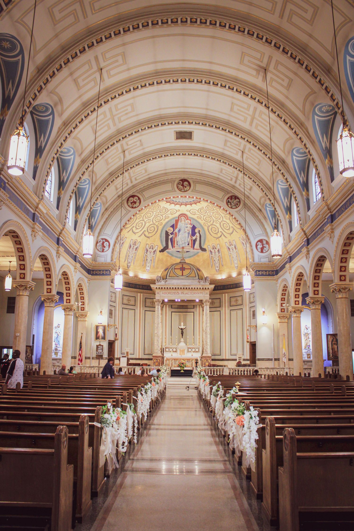 Interior view of ornate Catholic church with vaulted ceiling, decorative mosaics, and wooden pews along center aisle.