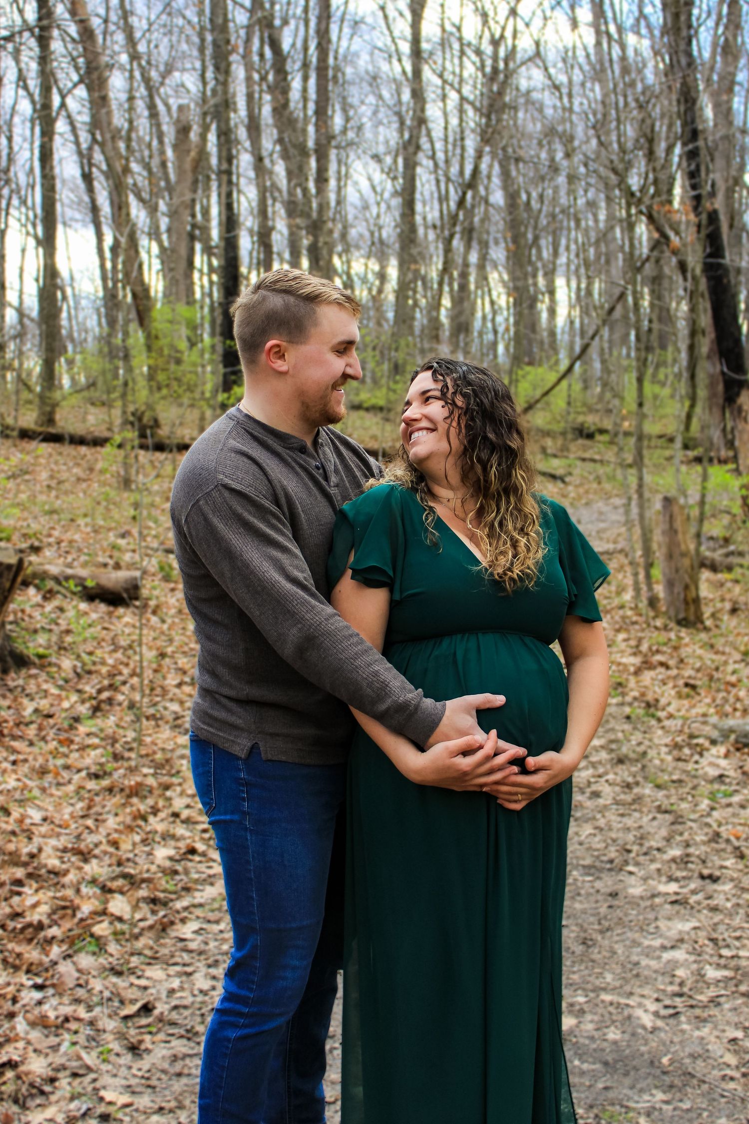 A couple shares a tender moment on a wooded trail as they pose for a maternity photo in fall.