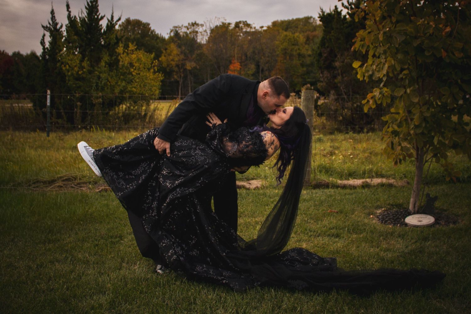 A person in black clothing performs a series of rolling movements on grass in an outdoor setting.