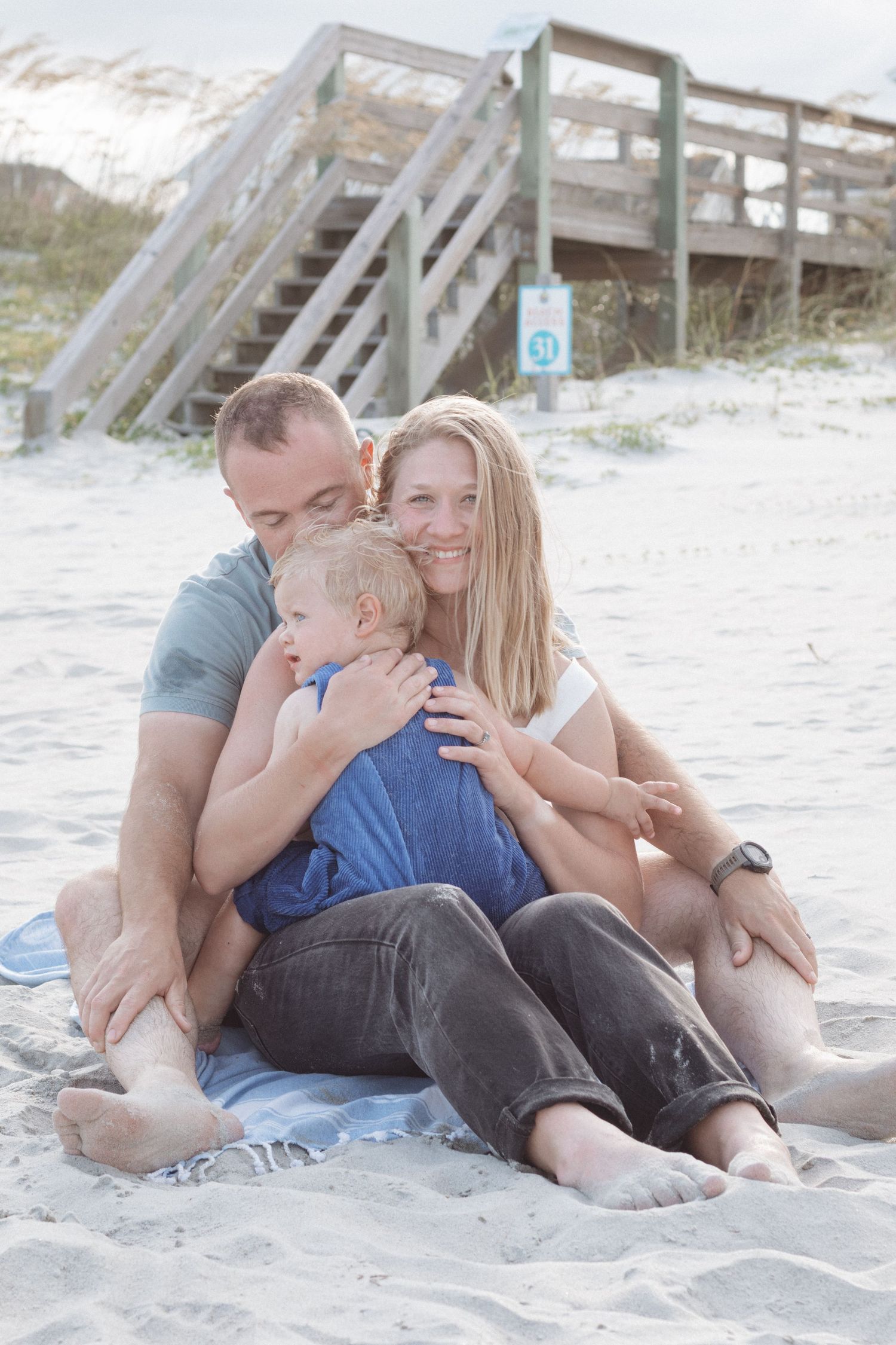 Family relaxing together on sandy beach during sunset photo session at coastal shore.