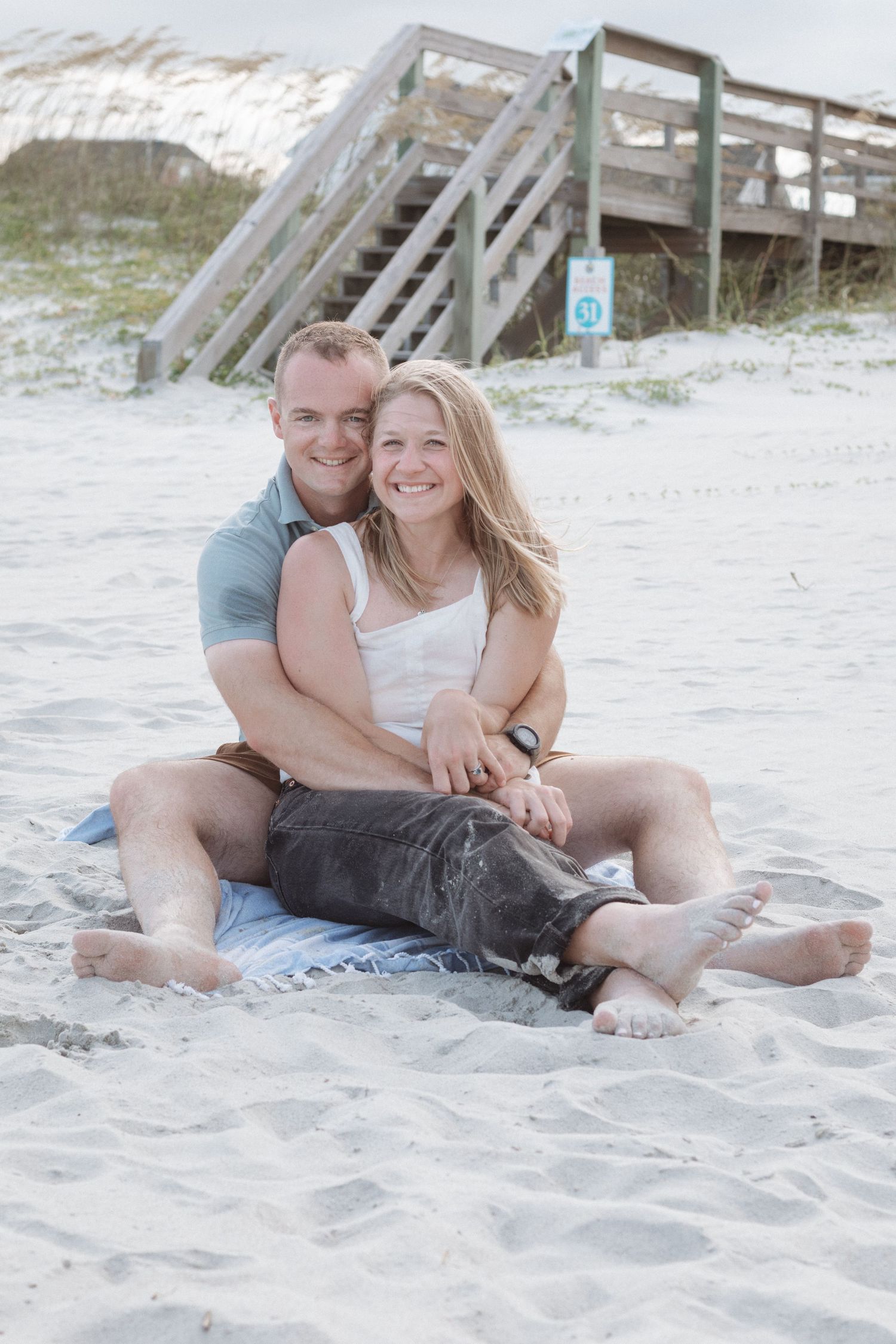 A couple sits together on a sandy beach with their dog on a sunny day, sharing intimate moments by the water.