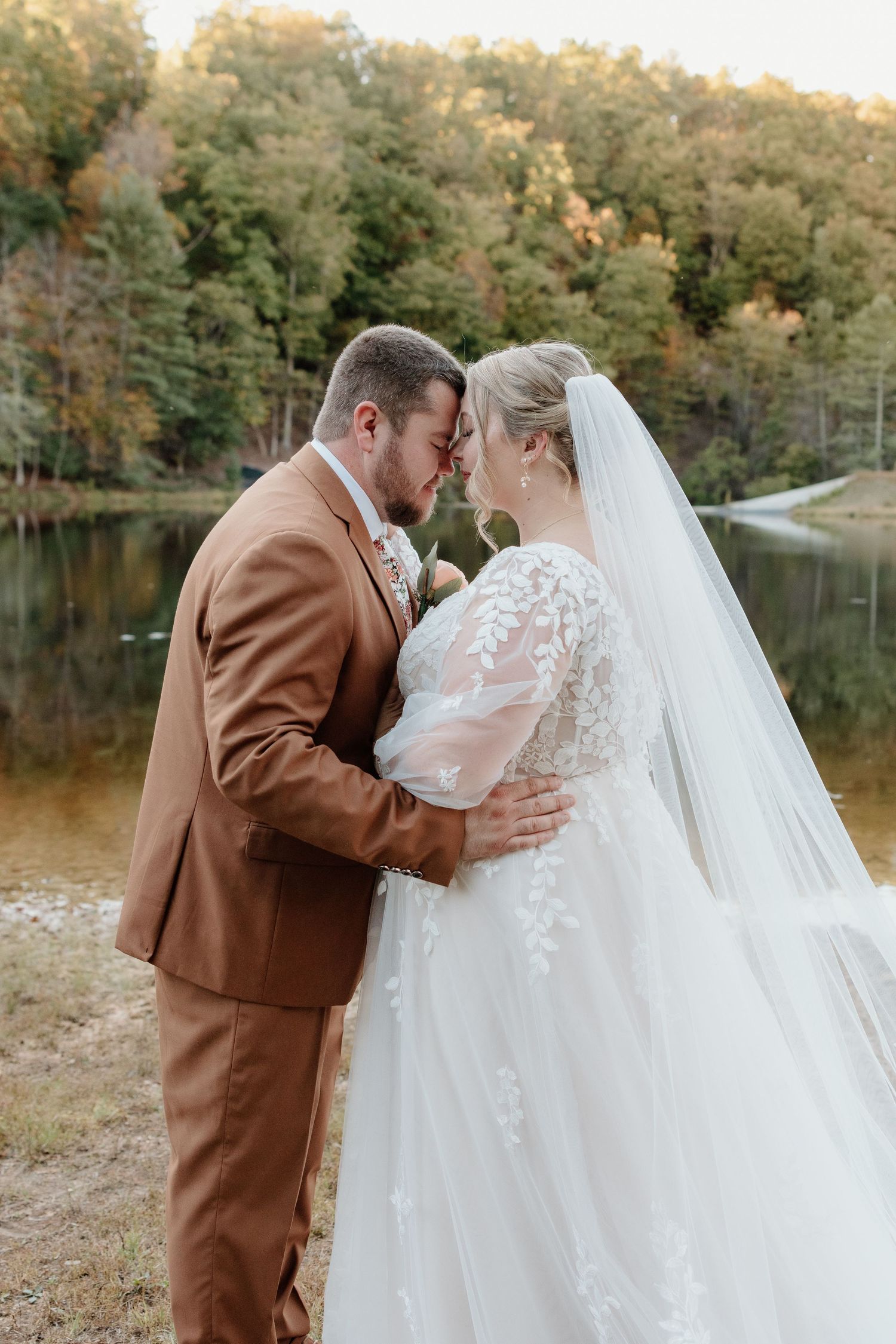 A romantic autumn wedding photoshoot by a serene lake with fall foliage creating a warm golden backdrop.