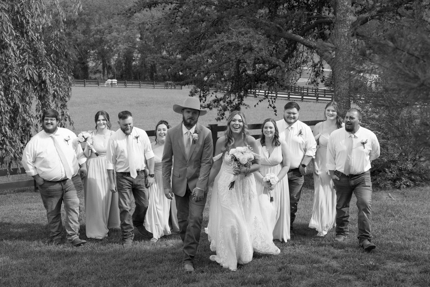 Black and white wedding party photo showing a line of people in formal attire outdoors.