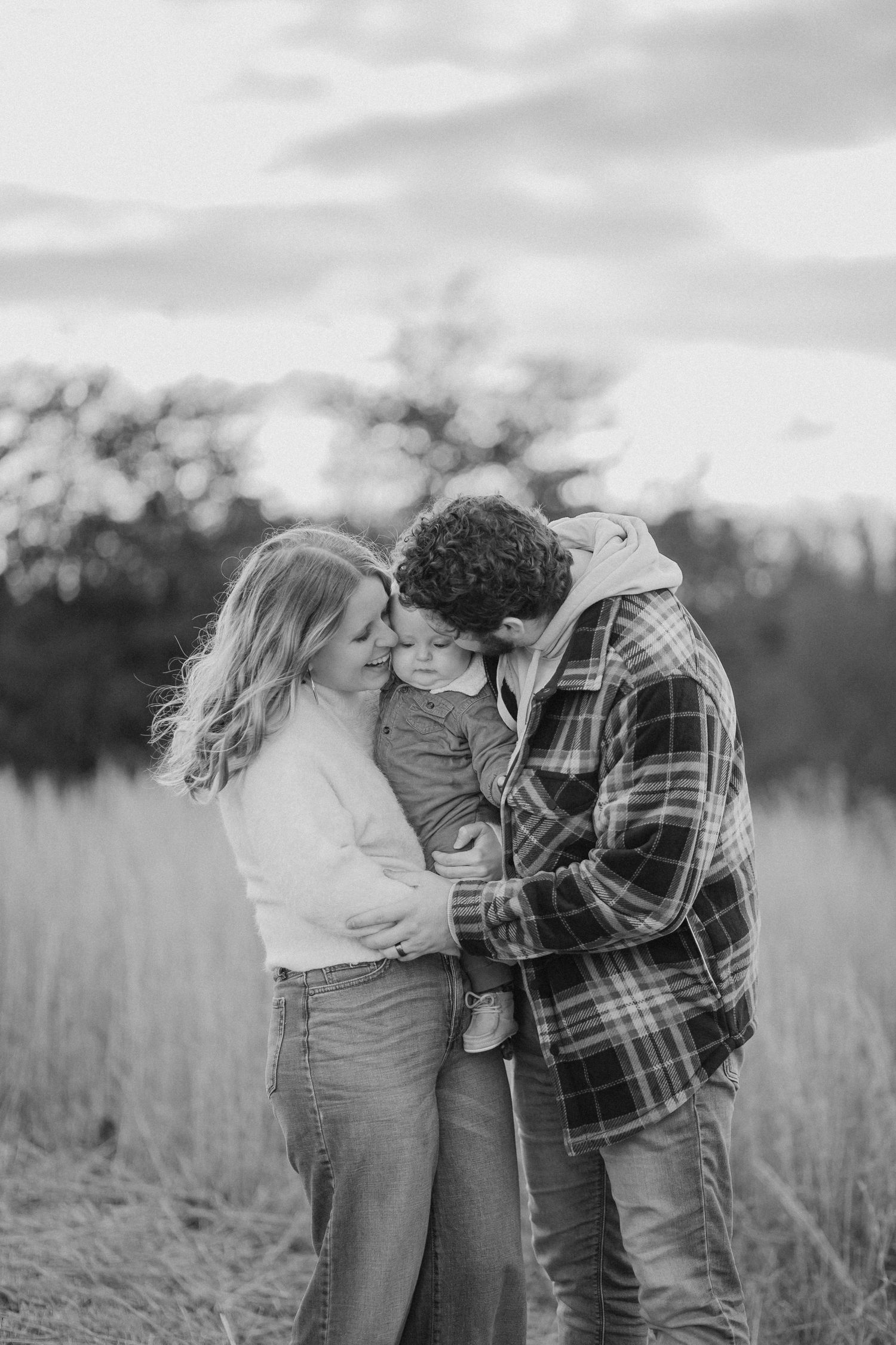 A family shares an intimate moment together in a serene field during a black and white photo session.