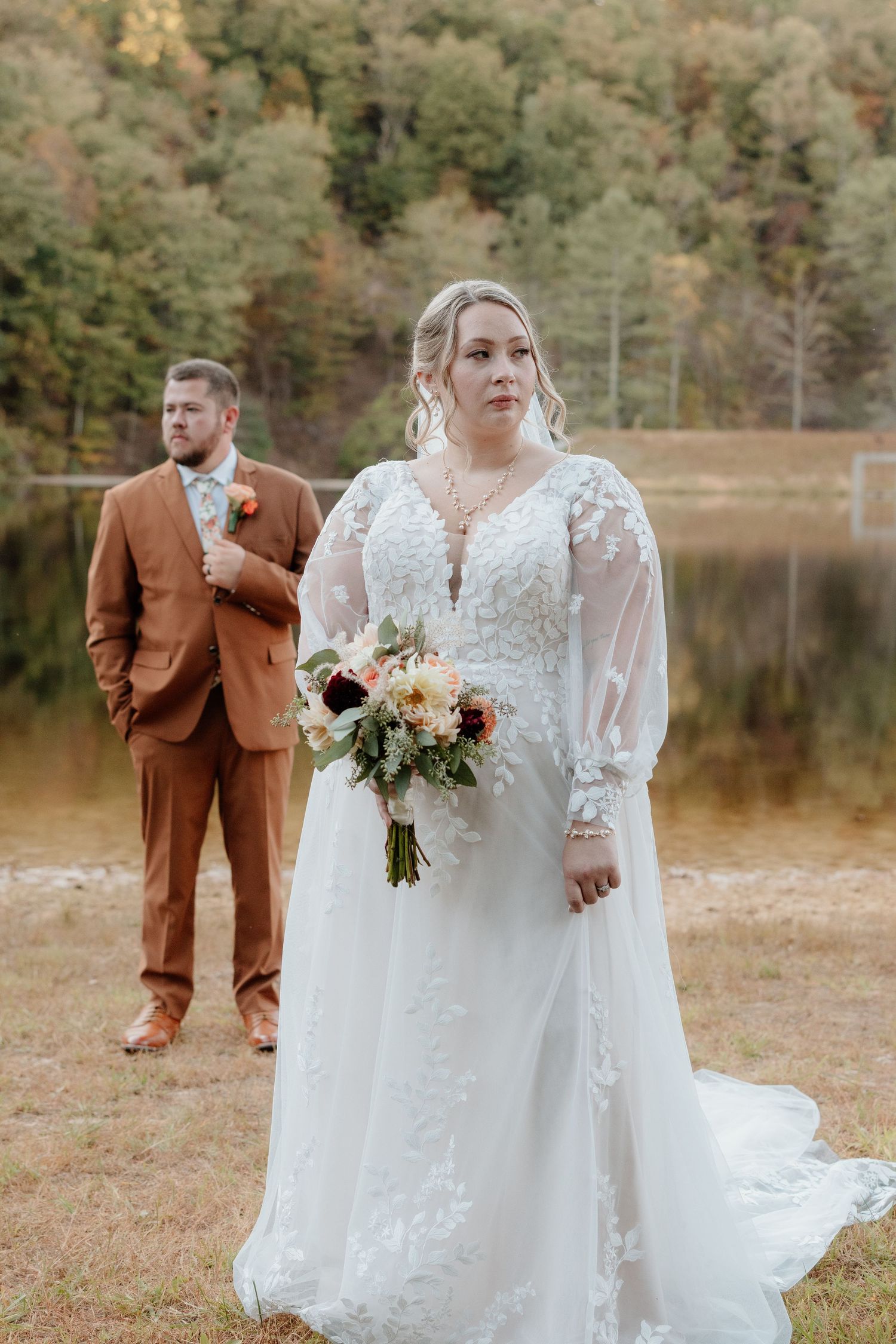 Wedding couple in brown suit and white dress photographed near autumn lake.