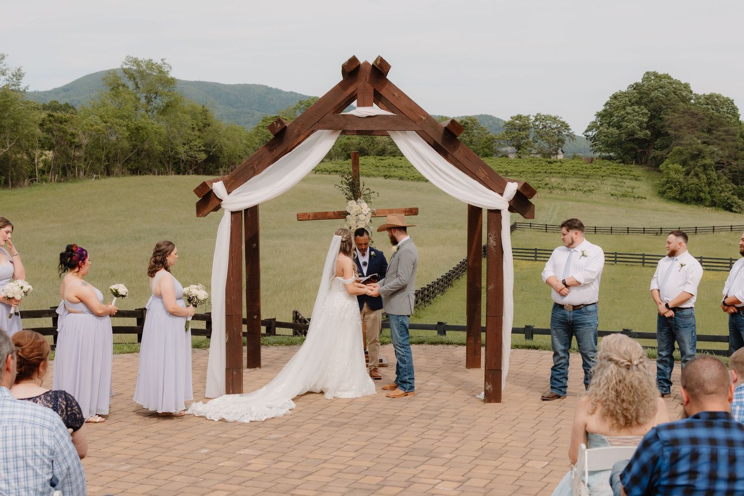 Wedding party poses in a rustic outdoor setting with mountains and wooden beams in the background.