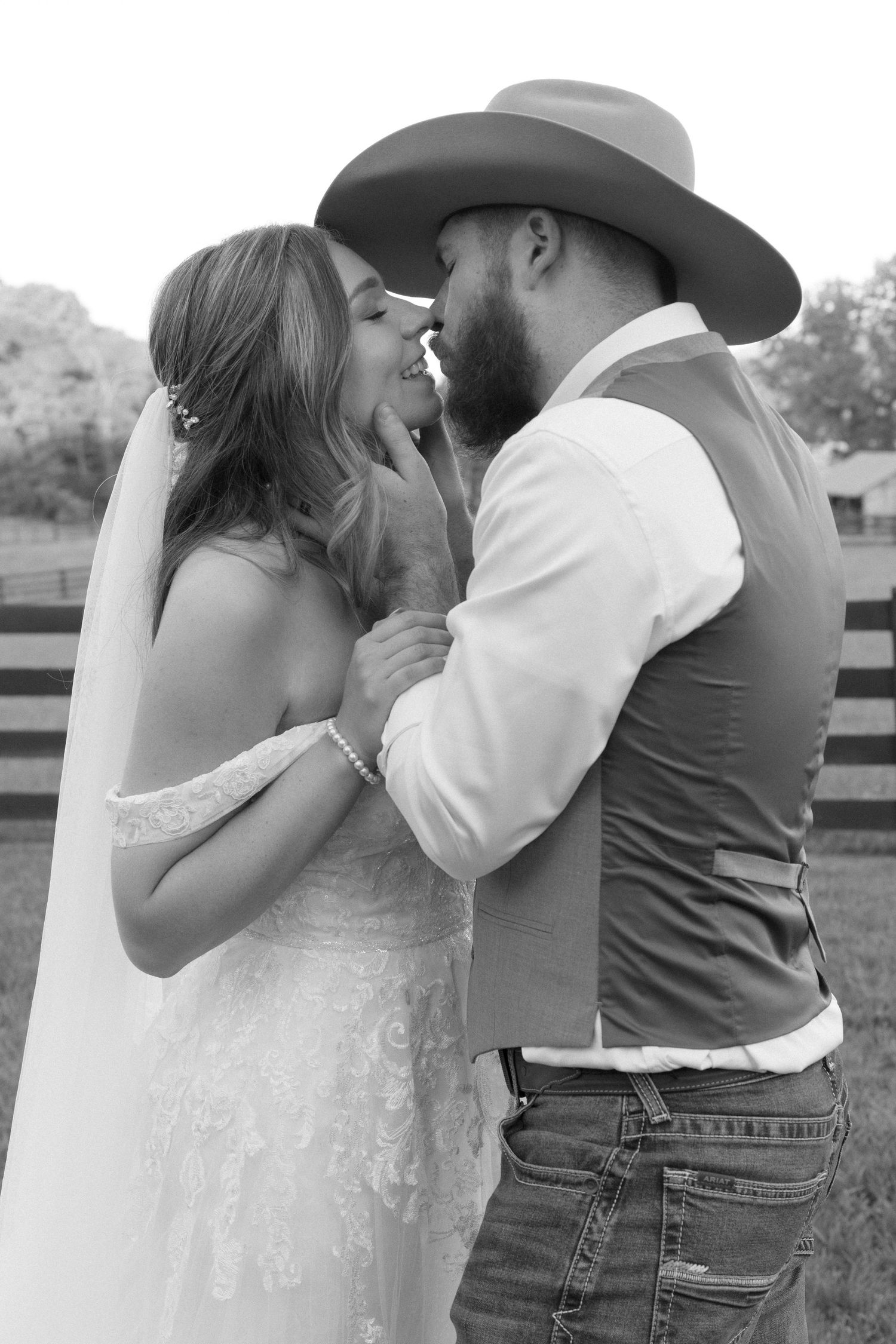 A romantic black and white photo series of a couple in western attire sharing intimate moments against a rustic fence.