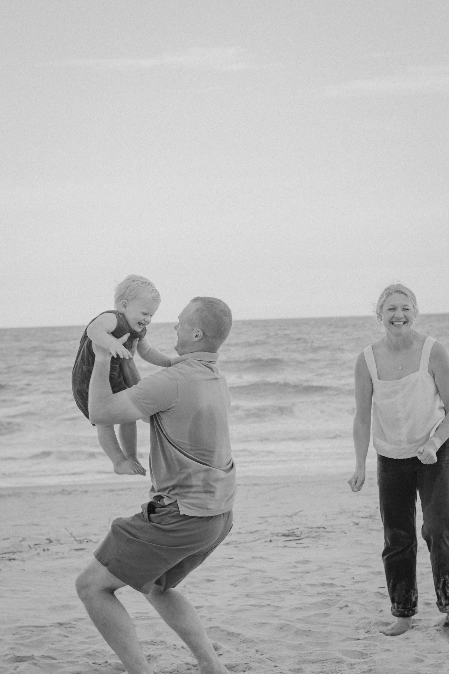 A joyful group plays and runs together along the beach shoreline in black and white photographs.
