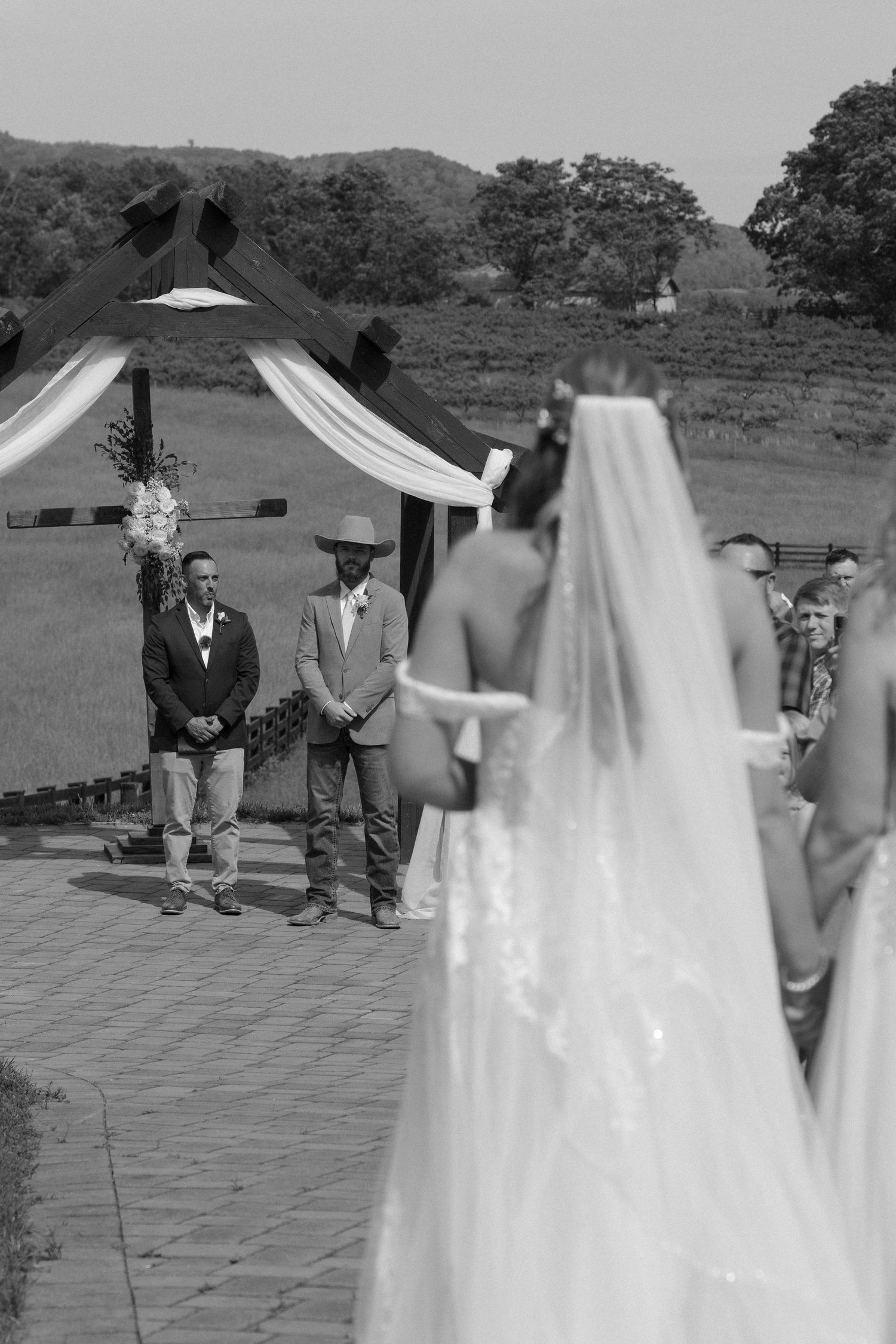 A black and white wedding ceremony photo sequence showing a couple and guests on a stone patio outdoors.