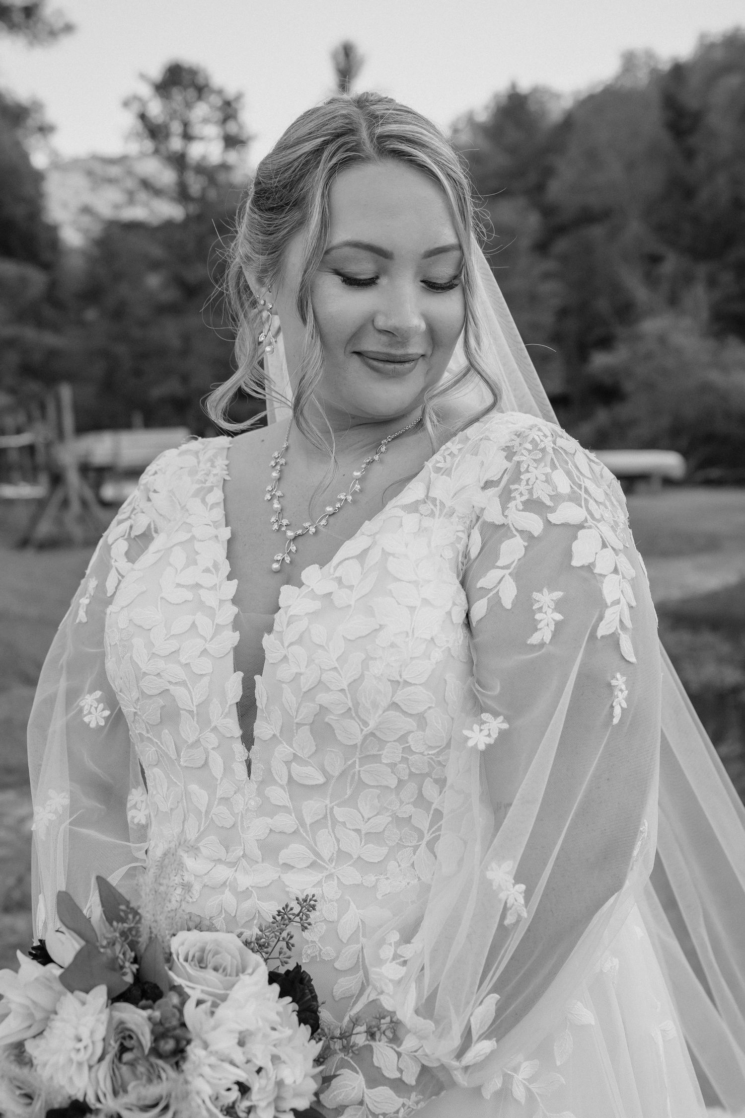Black and white portrait of a bride wearing an elegant lace wedding dress and holding a floral bouquet.