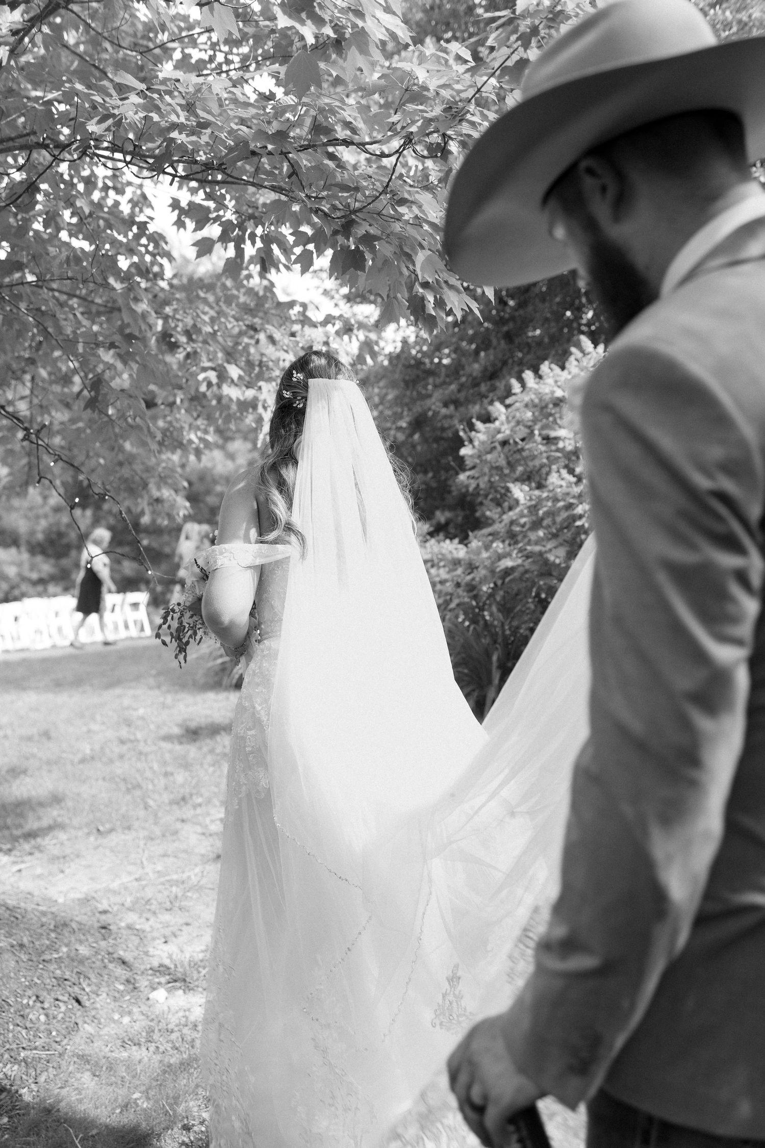 A couple in wedding attire walks through a garden setting captured in black and white photography.