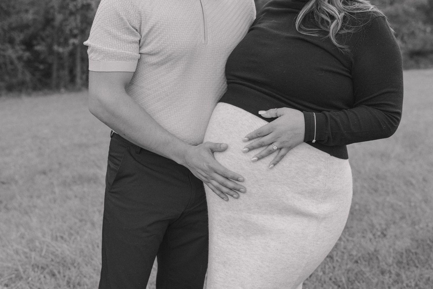 A couple in formal attire embraces outdoors during a romantic maternity photo session in black and white.