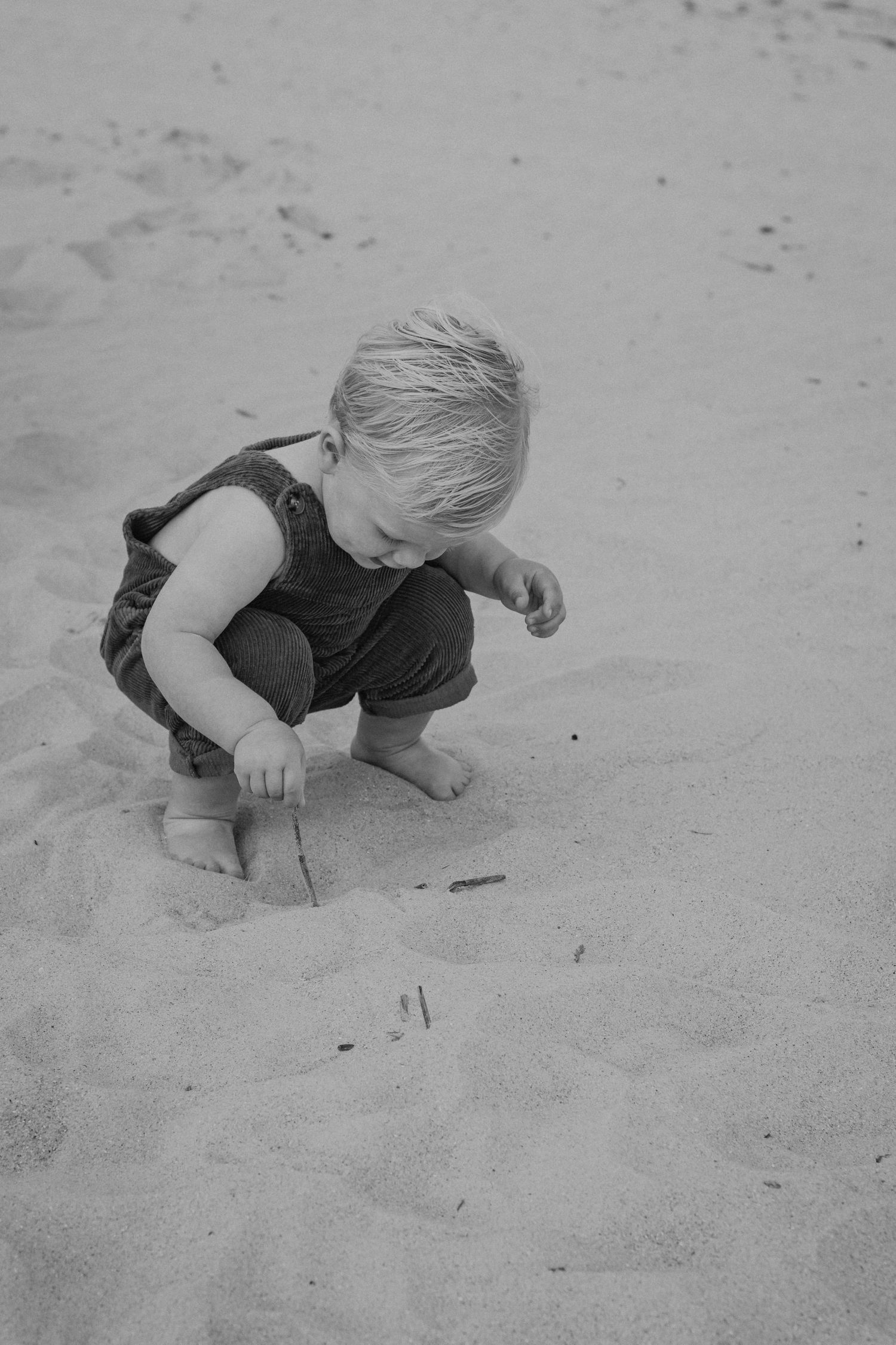 A child crouches down to explore and play in the sand at the beach, shown in a series of black and white photos.