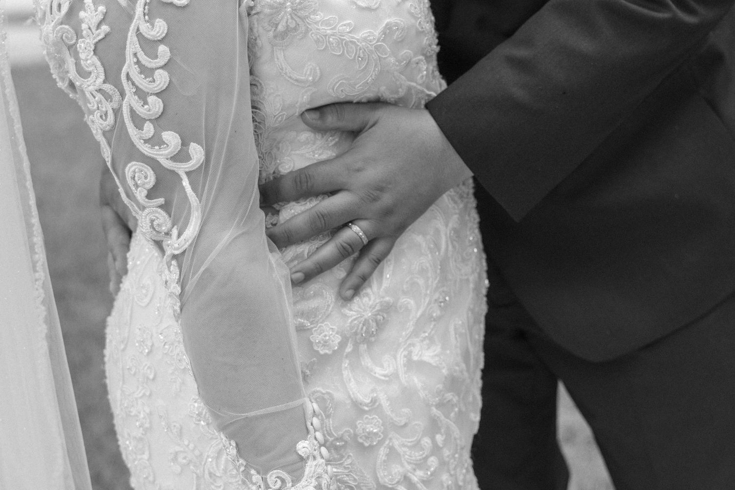 Black and white wedding photo of groom's hand resting on bride's lace wedding dress waist.