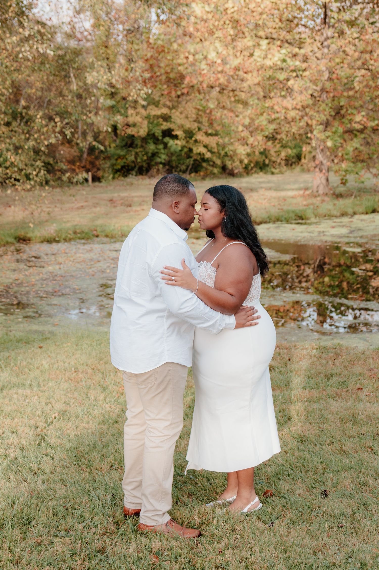 A couple in white outfits share romantic moments while dancing together on grassy terrain during a photo session.