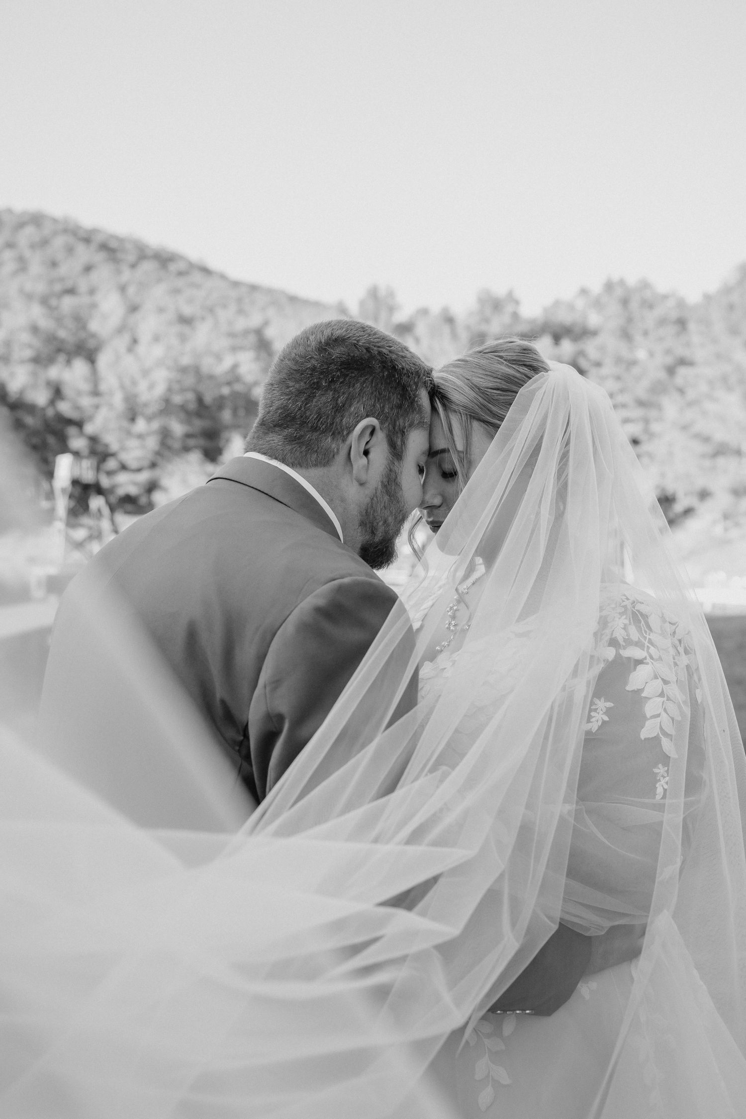 Black and white wedding photos showing close-up shots of a bride and groom embracing with flowing veil details.