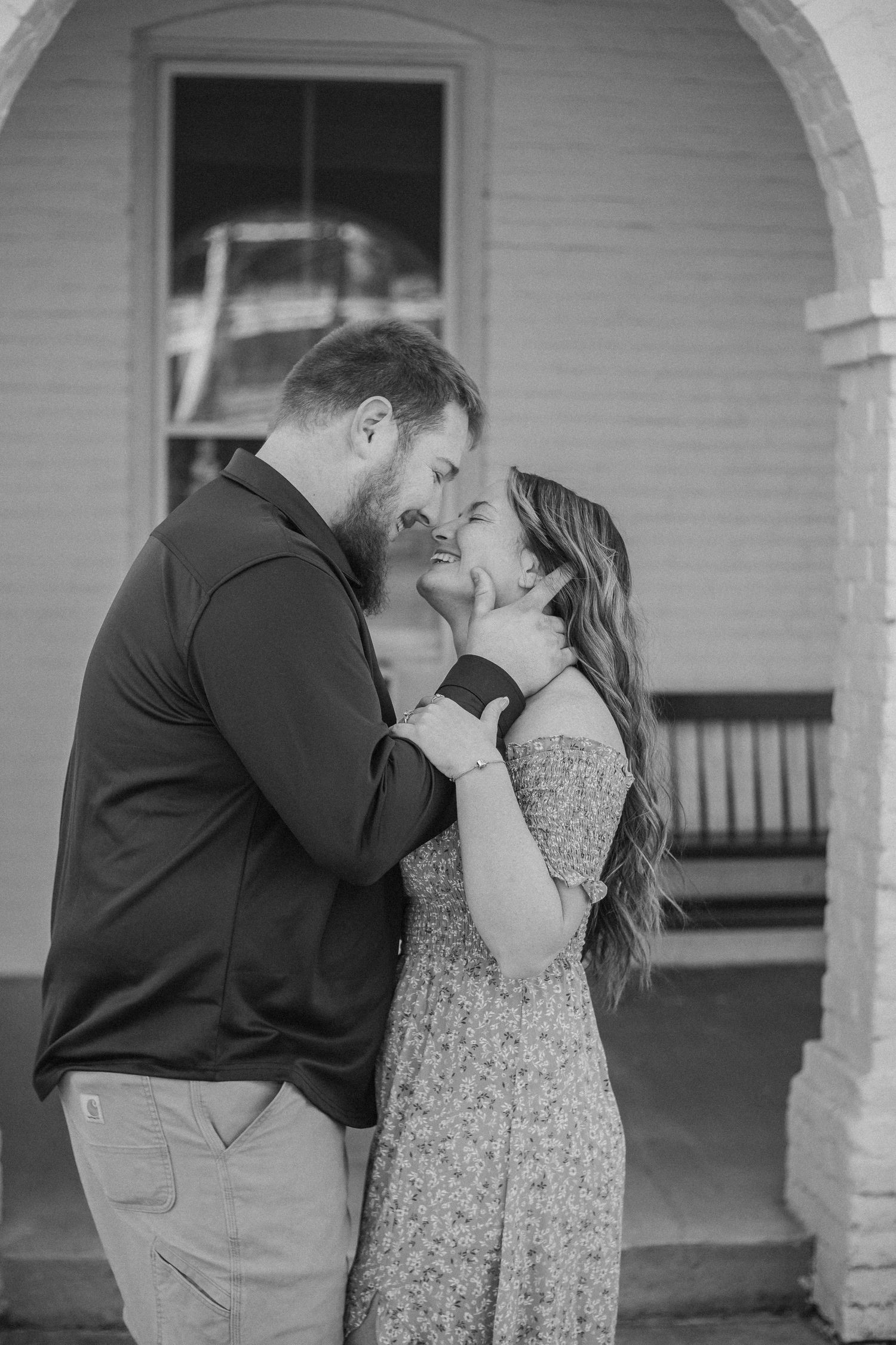 A couple shares an intimate moment on a porch in a black and white photo.