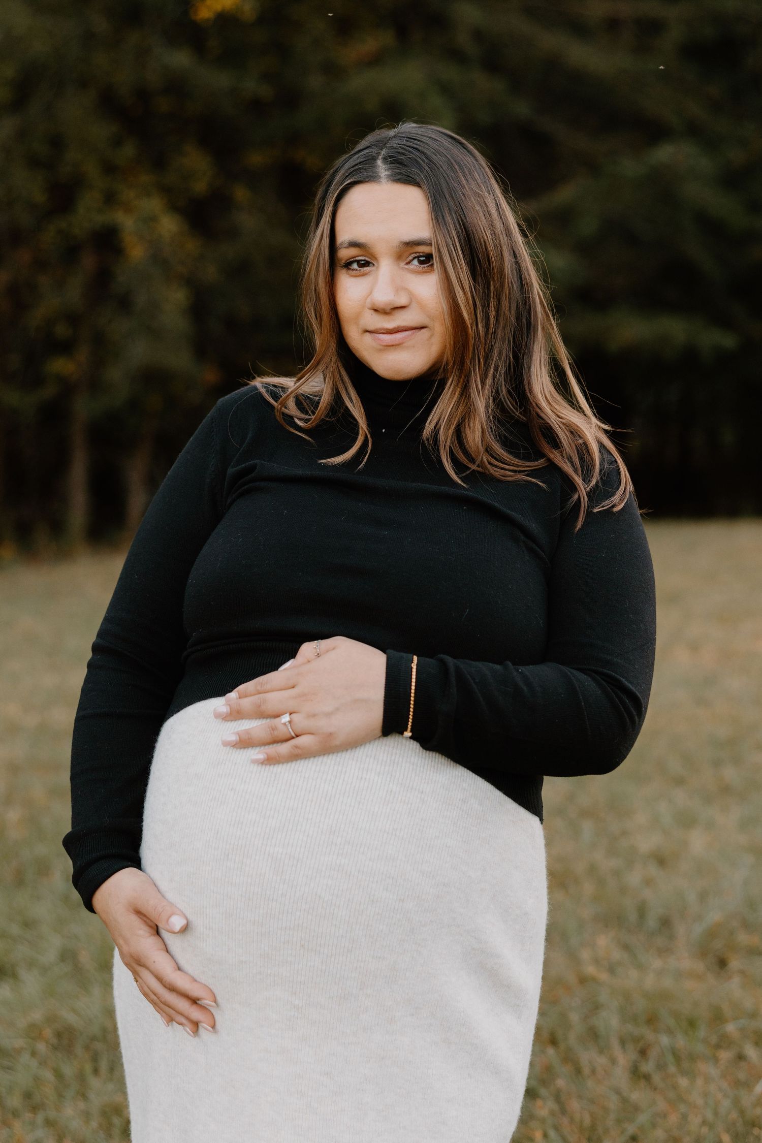 A series of intimate maternity photos showing a woman in black holding her baby bump against an autumn backdrop.
