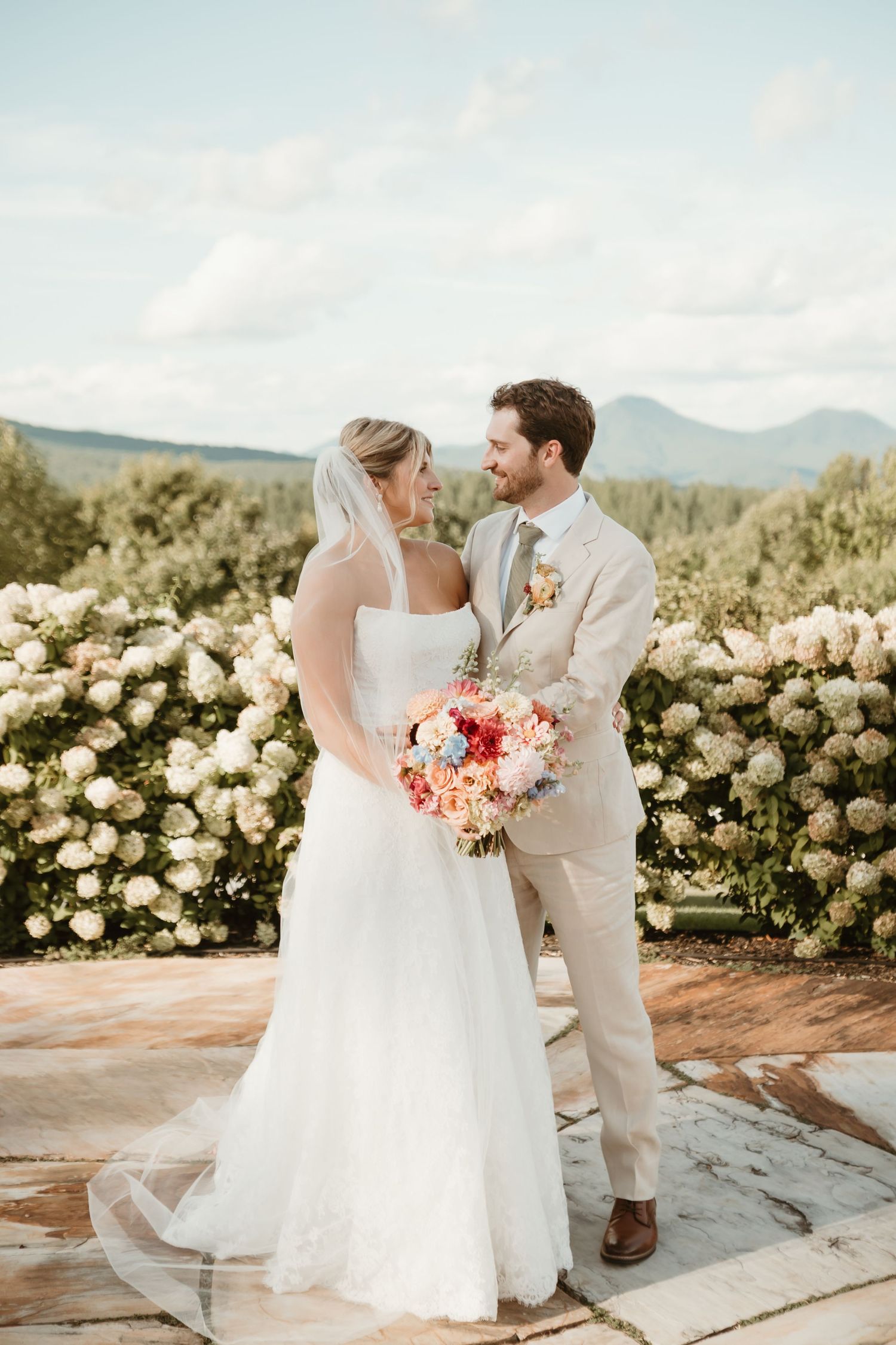 Bride and groom share a romantic moment in front of white hydrangeas with mountain views on their wedding day.