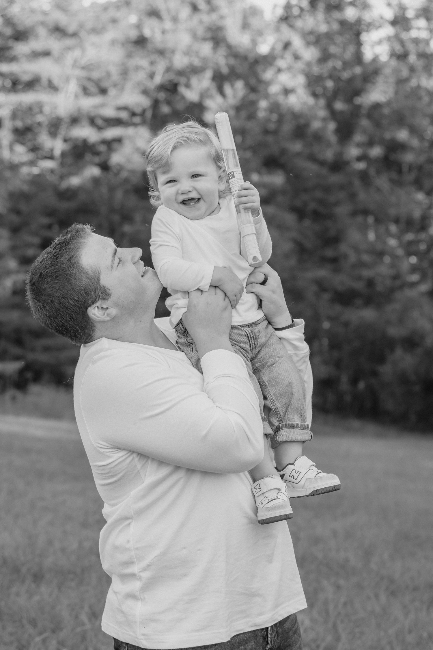 A parent in a white shirt lifts and plays with a small child outdoors in a series of candid black and white photos.