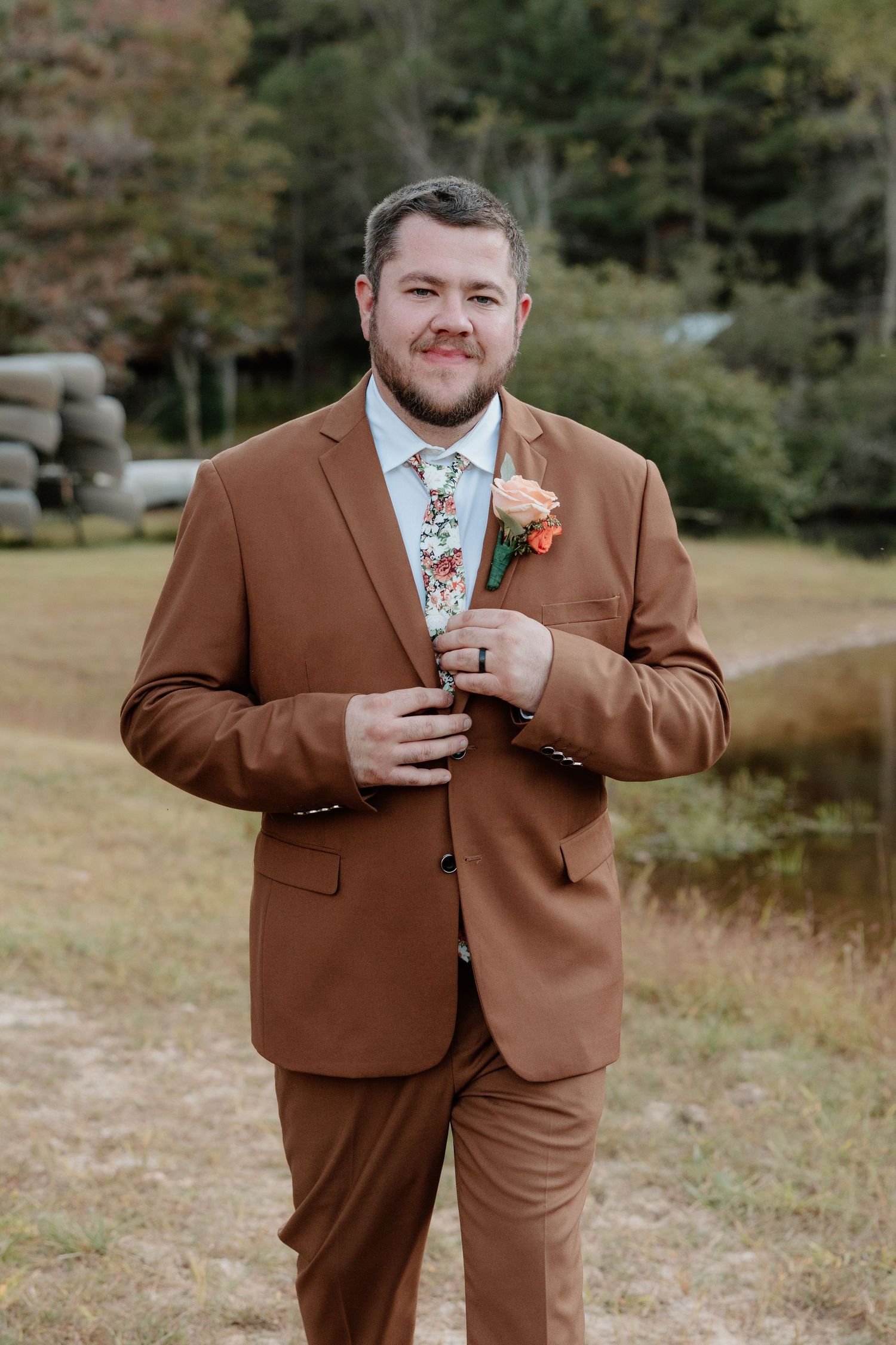 Groom in brown suit jacket holding letter during first look wedding photos outdoors.